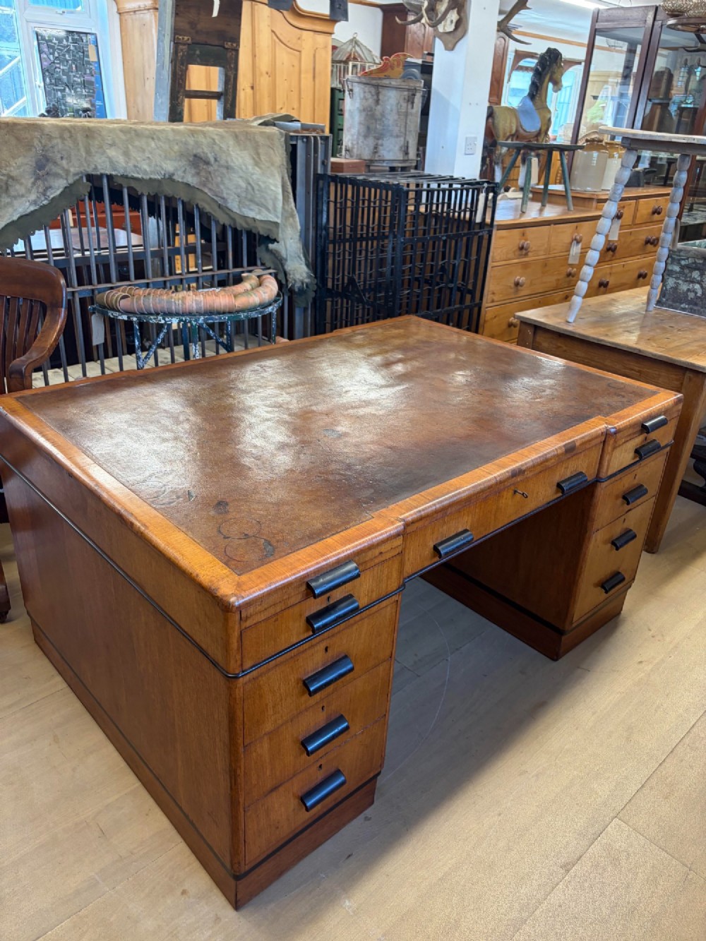 A large Art Deco walnut partner desk featuring a brown leather inset top and black horizontal drawer handles.