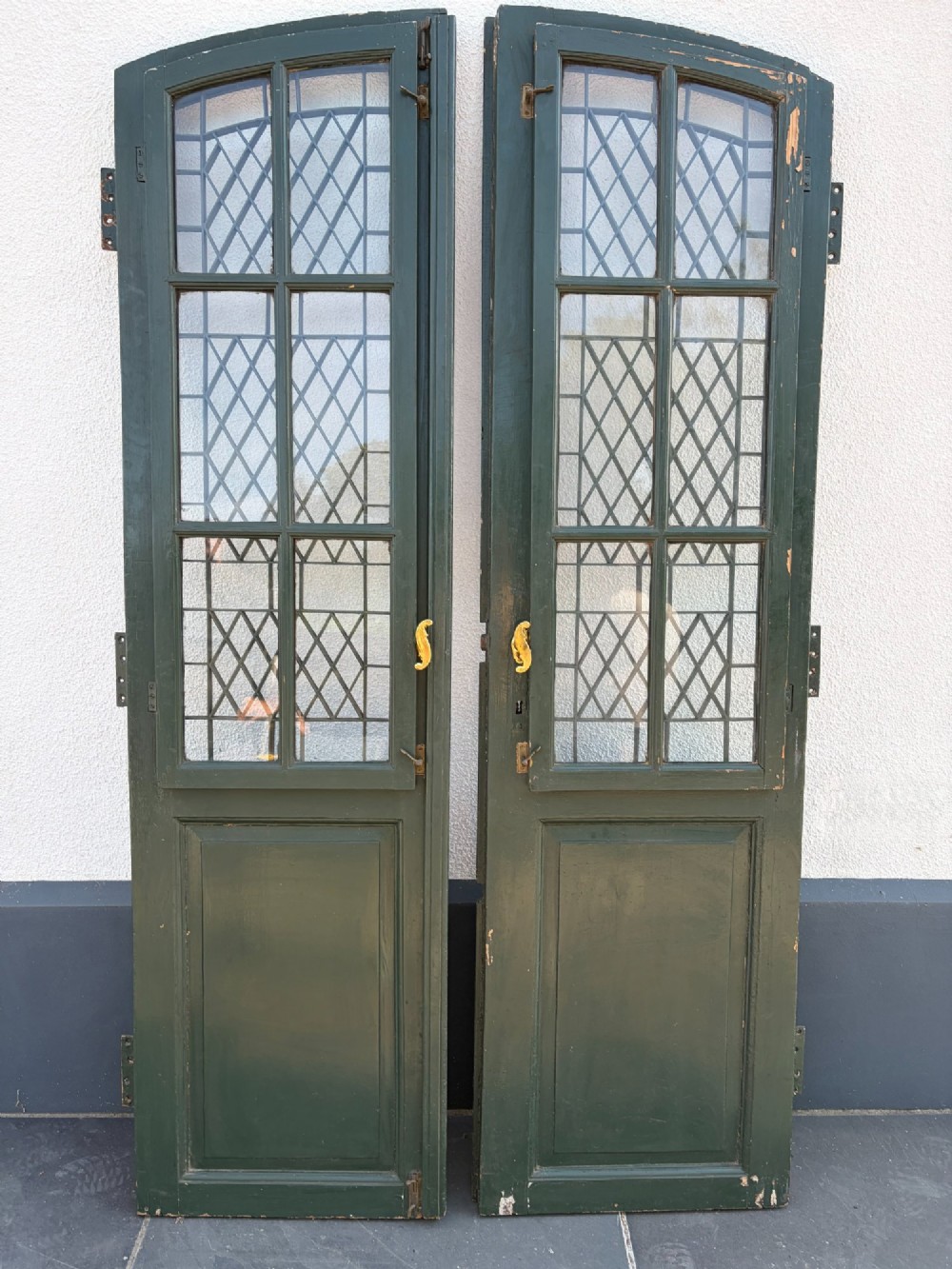 A pair of dark green painted pine double doors featuring arched tops, iron lattice grilles, and opening glazed window frames above solid lower timber panels. View III