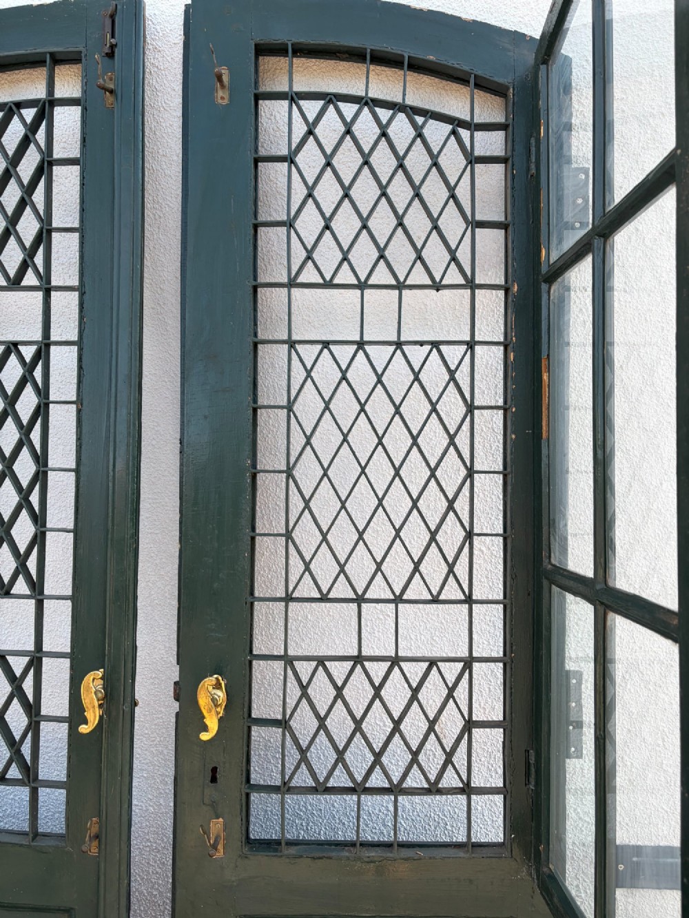 A pair of dark green painted pine double doors featuring arched tops, iron lattice grilles, and opening glazed window frames above solid lower timber panels. View IV