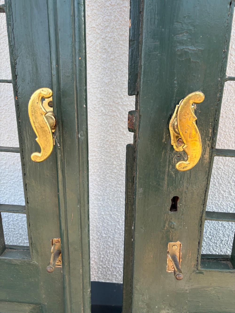 A pair of dark green painted pine double doors featuring arched tops, iron lattice grilles, and opening glazed window frames above solid lower timber panels. View VI