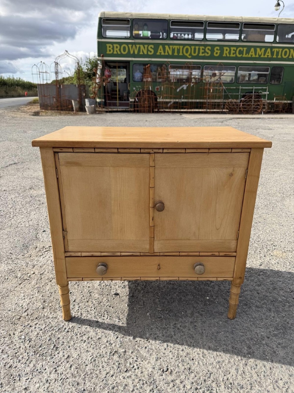 An early 19th-century light pine cupboard featuring double panelled doors, a single lower drawer, and carved faux bamboo frame trim and turned legs.