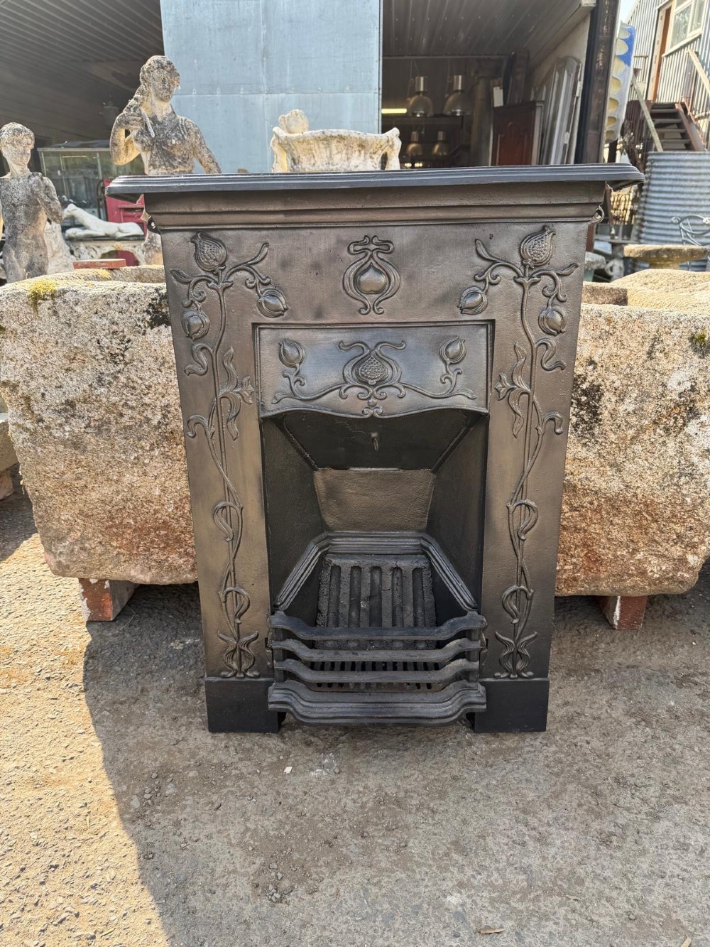 An antique Victorian cast iron combination fireplace featuring relief floral tendrils and seed pod motifs with an integrated grate and mantel shelf.