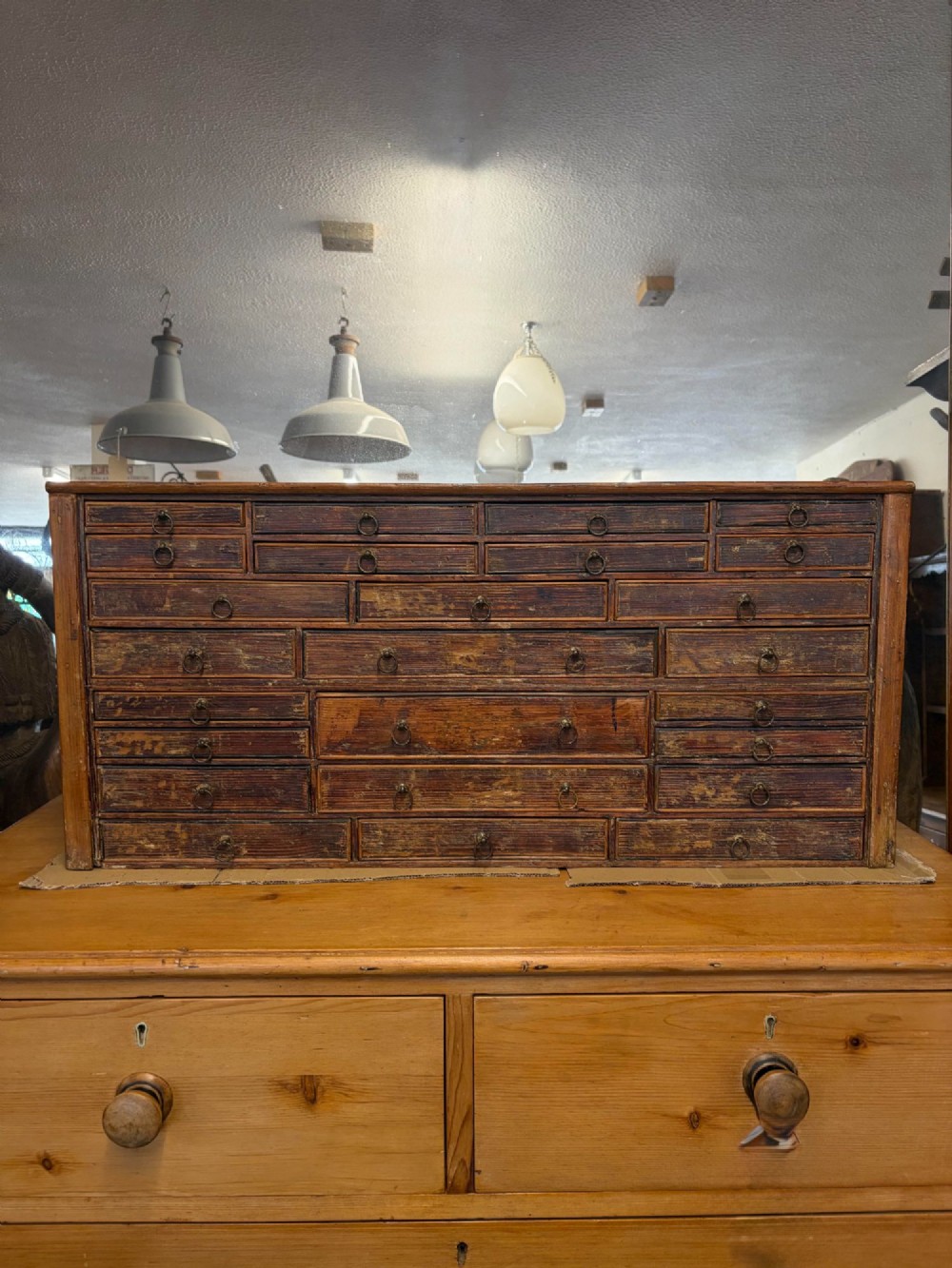 A 19th-century wooden bank of twenty-five individual drawers featuring metal ring pulls and a distressed dark finish.