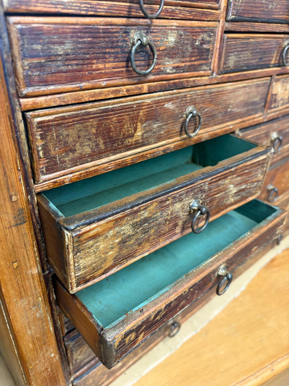 A 19th-century wooden bank of twenty-five individual drawers featuring metal ring pulls and a distressed dark finish. View VIII