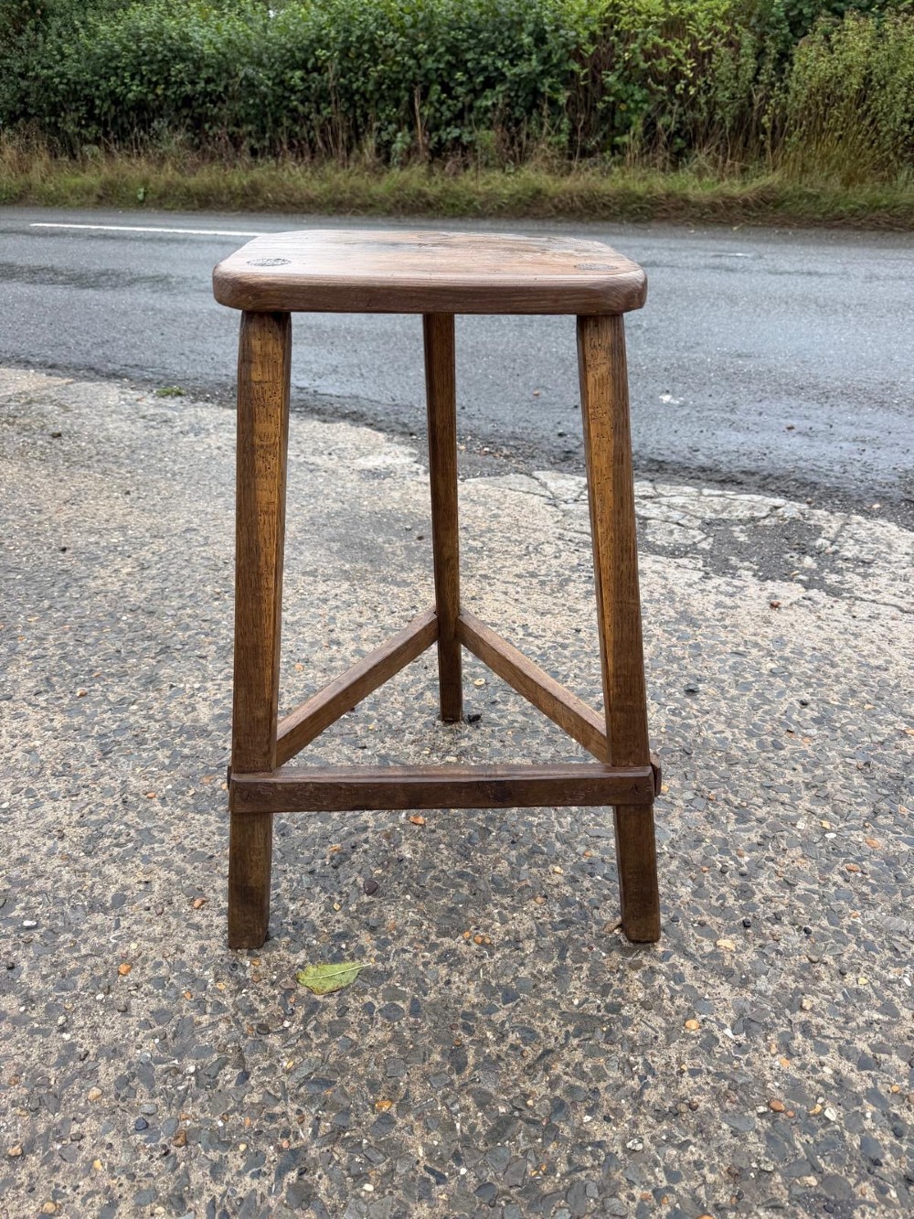 A three-legged dark brown timber artisan stool featuring exposed wedged tenons on the seat surface and triangular cross stretchers. View II