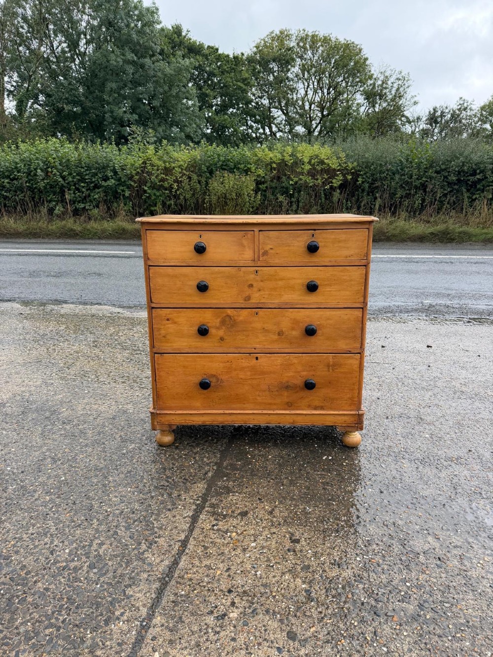 A Victorian pine chest of drawers featuring two small drawers above three graduated long drawers, detailed with dark turned knobs and resting on turned bun feet.