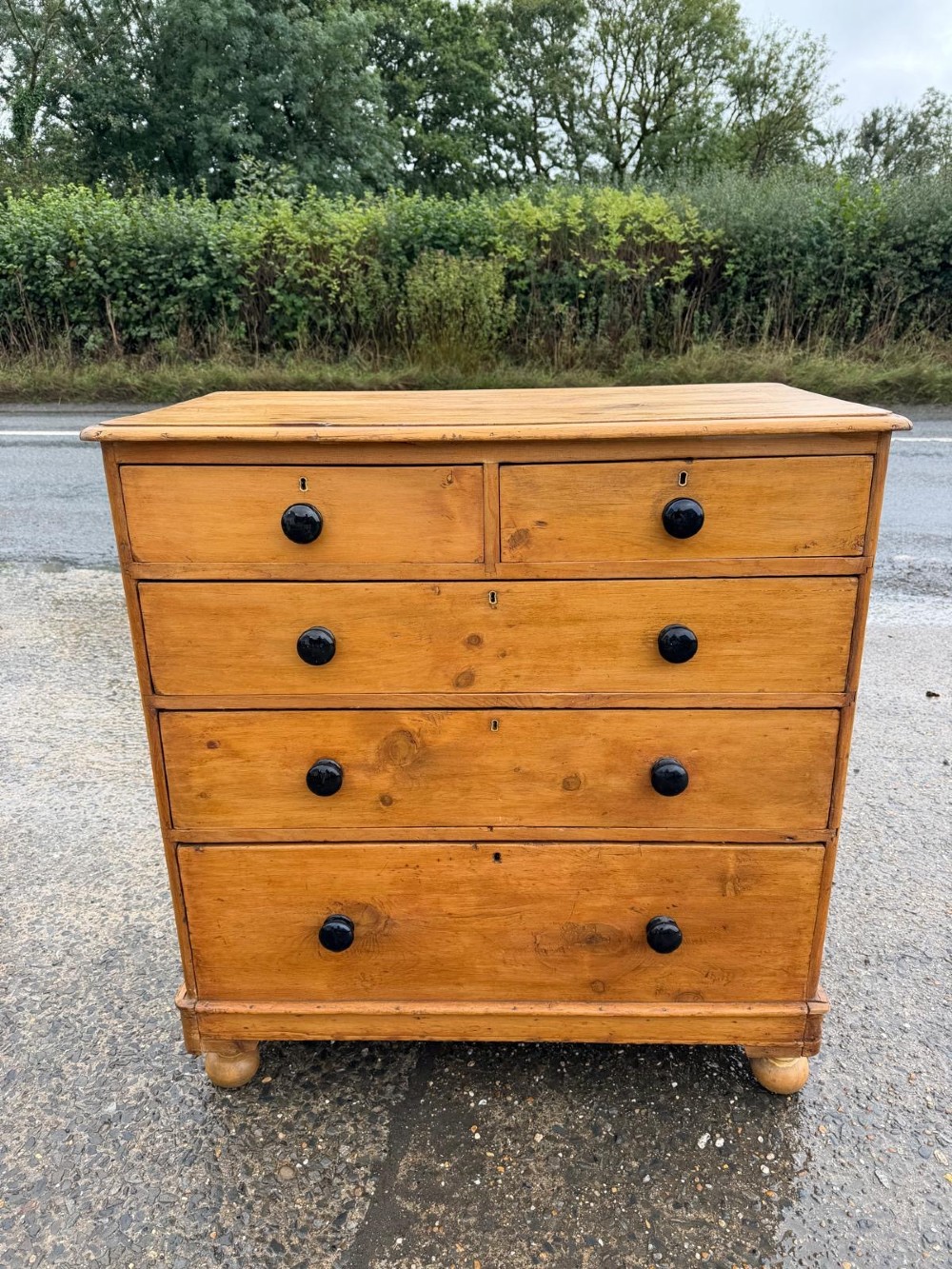 A Victorian pine chest of drawers featuring two small drawers above three graduated long drawers, detailed with dark turned knobs and resting on turned bun feet. View II