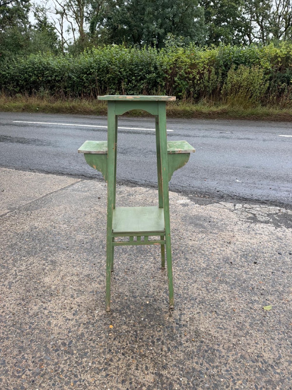 A tall, slender green painted timber plant stand circa 1900, featuring four tiered platforms and arched support brackets.