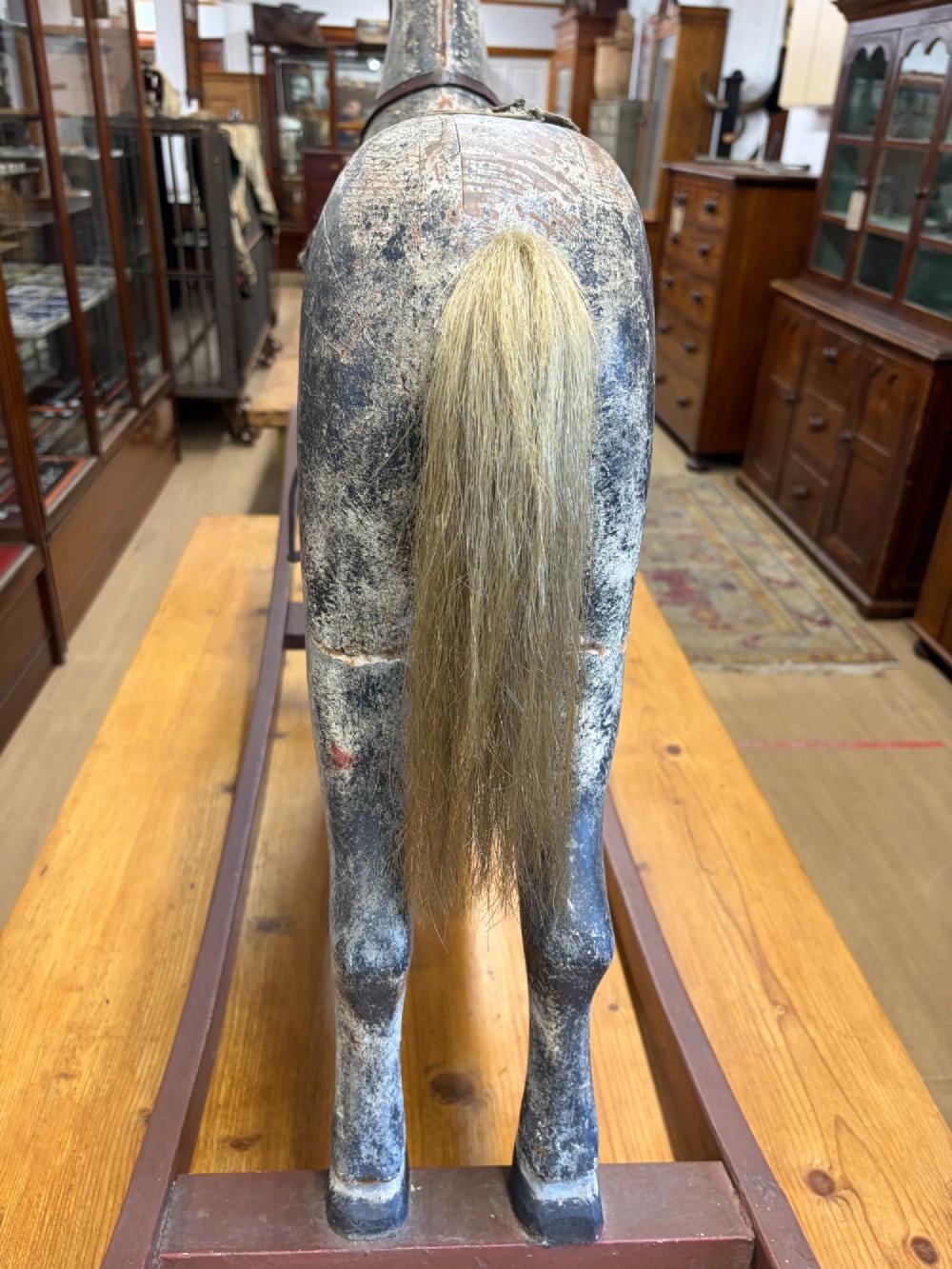 A 19th-century carved wooden primitive rocking horse with weathered paint, leather tack, and dark reddish-brown bow rockers. View V