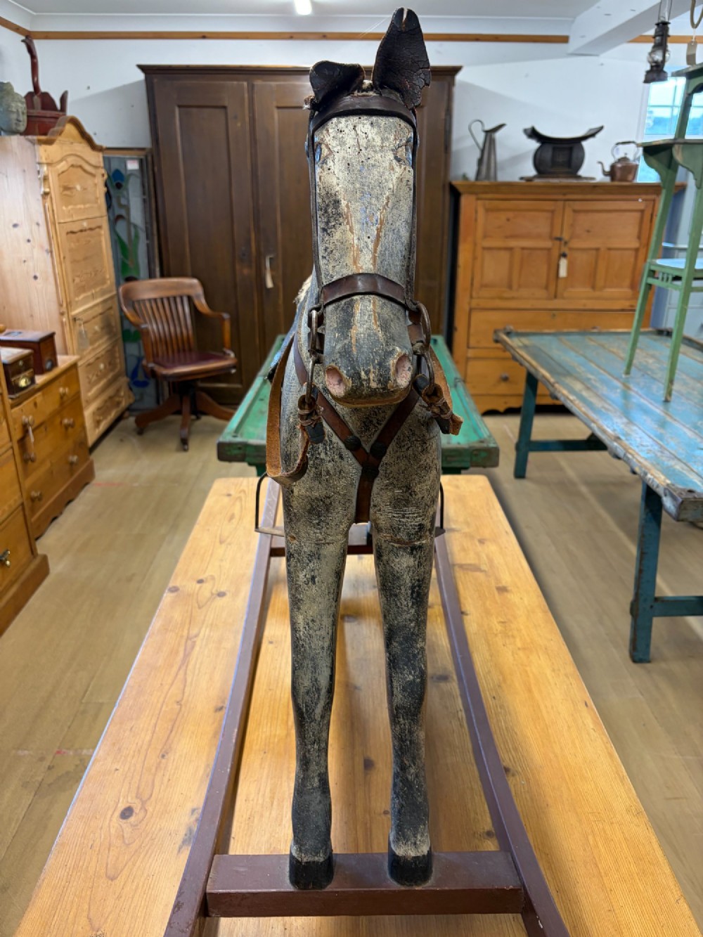 A 19th-century carved wooden primitive rocking horse with weathered paint, leather tack, and dark reddish-brown bow rockers. View X