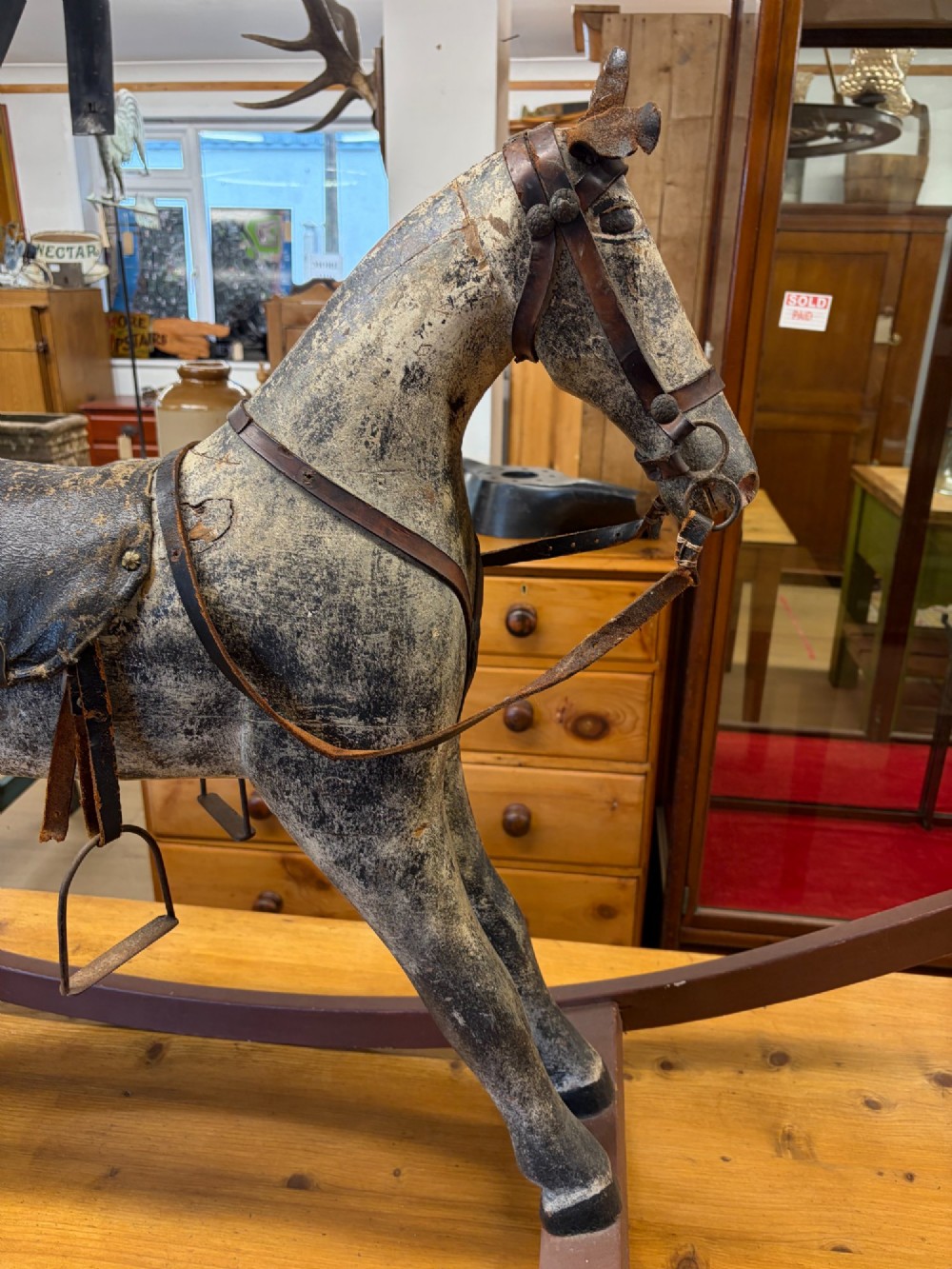 A 19th-century carved wooden primitive rocking horse with weathered paint, leather tack, and dark reddish-brown bow rockers. View XII