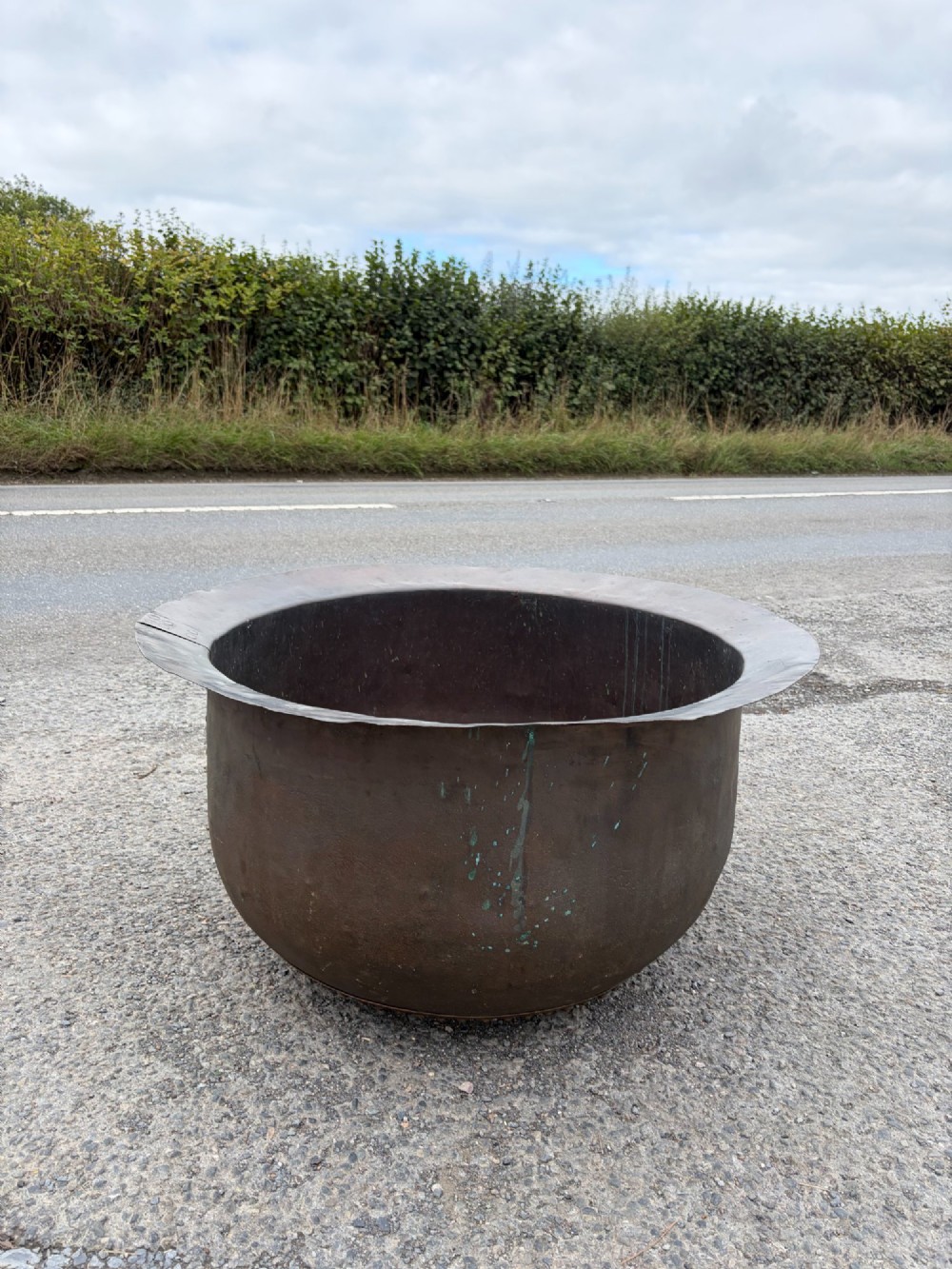 A large 19th-century copper pot featuring a wide flared rim, deep rounded vessel, and dark oxidized copper patina with subtle verdigris details.