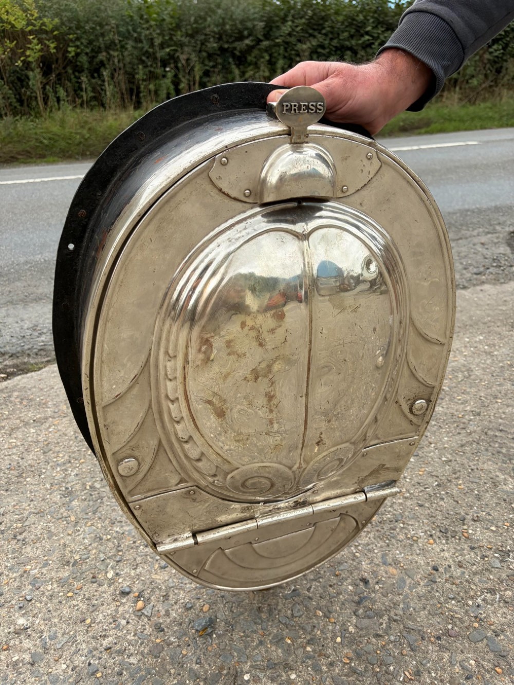 An oval silver-plated railway carriage folding sink featuring relief scrollwork, a press-button top mechanism, and exposed brass pipe fittings. View II