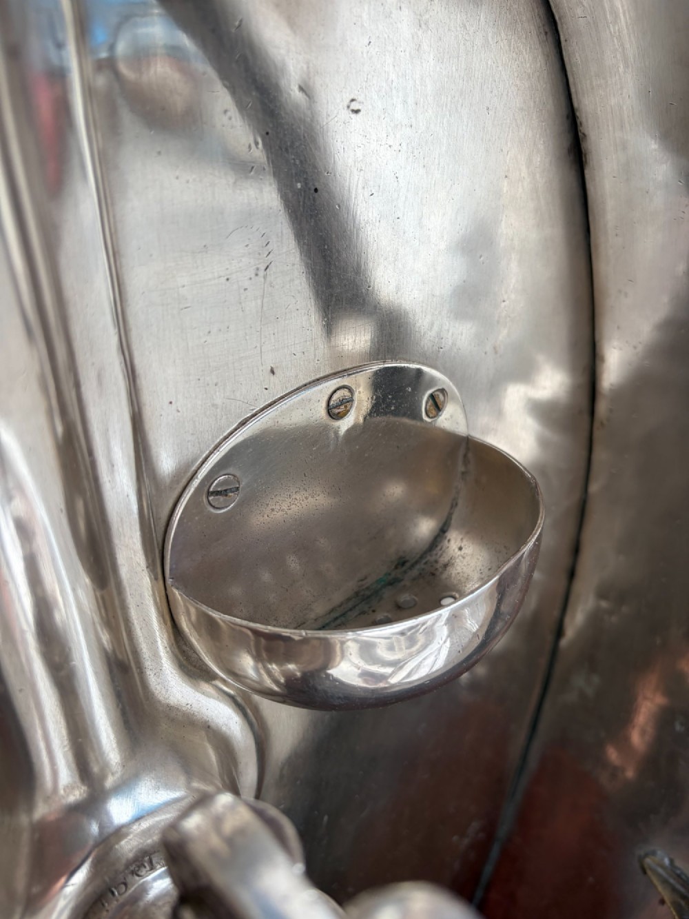 An oval silver-plated railway carriage folding sink featuring relief scrollwork, a press-button top mechanism, and exposed brass pipe fittings. View VIII