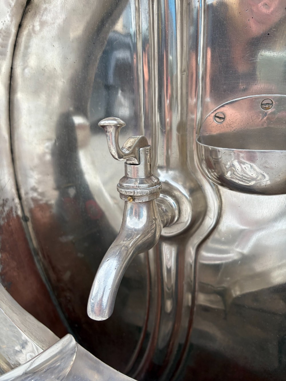 An oval silver-plated railway carriage folding sink featuring relief scrollwork, a press-button top mechanism, and exposed brass pipe fittings. View IX