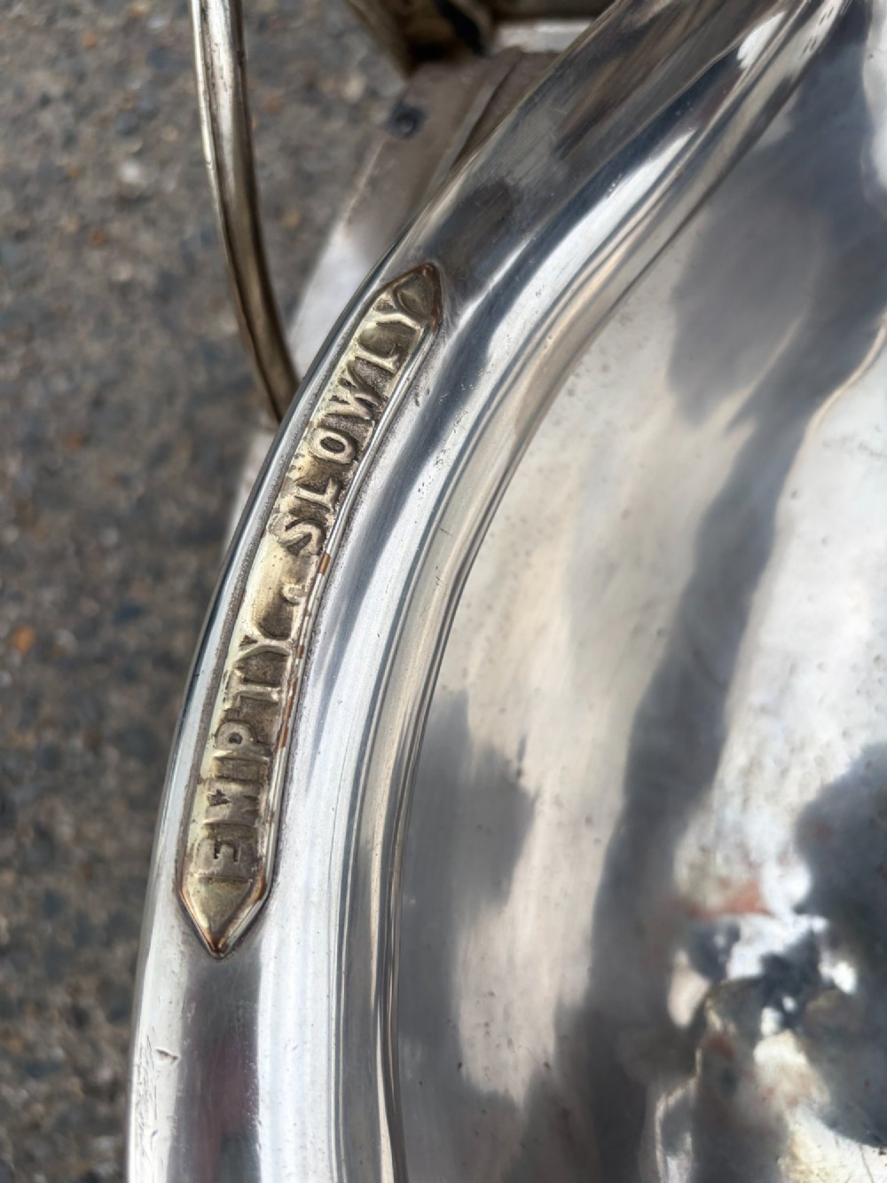 An oval silver-plated railway carriage folding sink featuring relief scrollwork, a press-button top mechanism, and exposed brass pipe fittings. View X