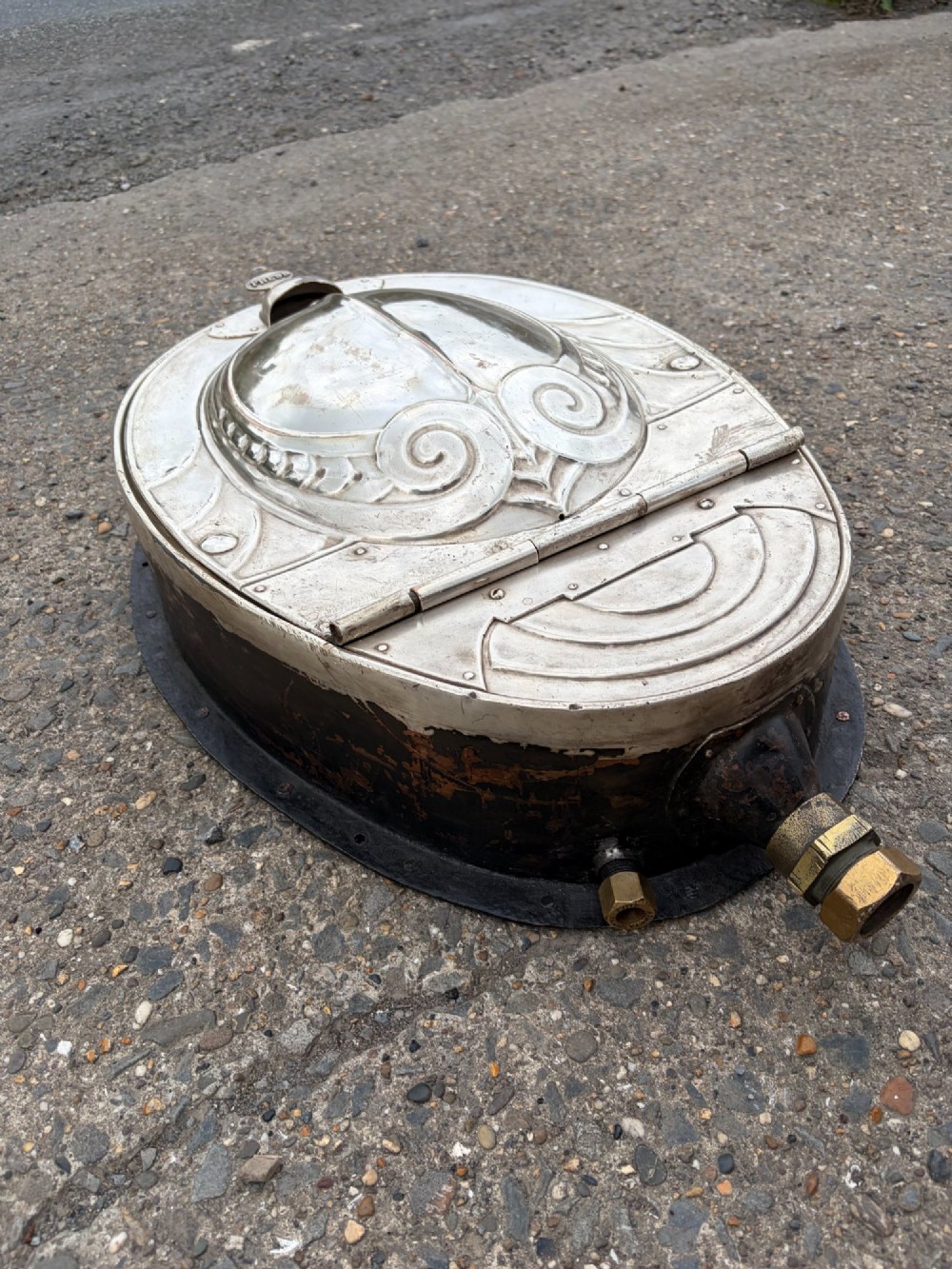 An oval silver-plated railway carriage folding sink featuring relief scrollwork, a press-button top mechanism, and exposed brass pipe fittings. View XI