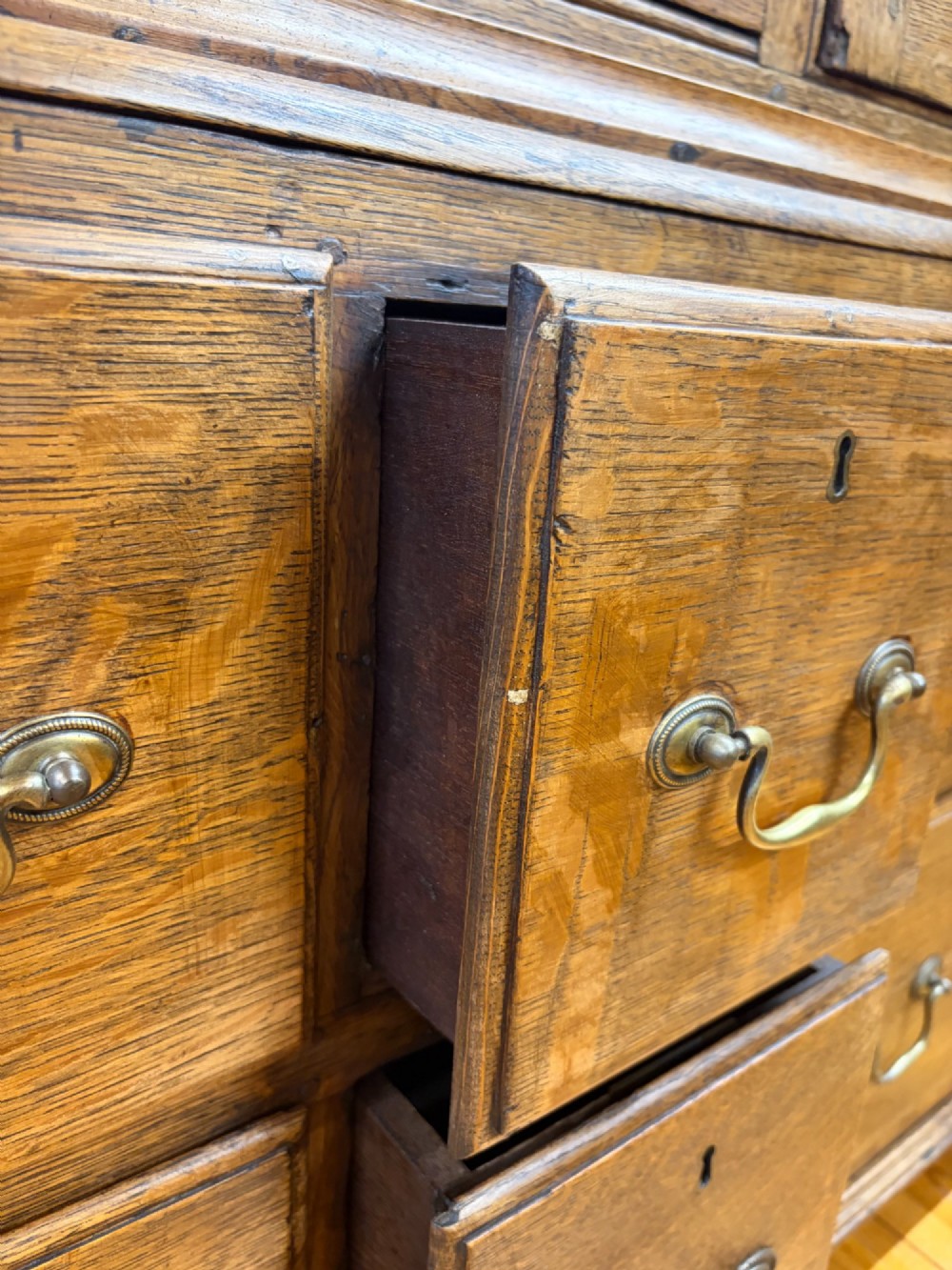 An antique George III oak housekeepers cupboard with arched fielded panels on the top doors above a base of drawers with brass handles. View II