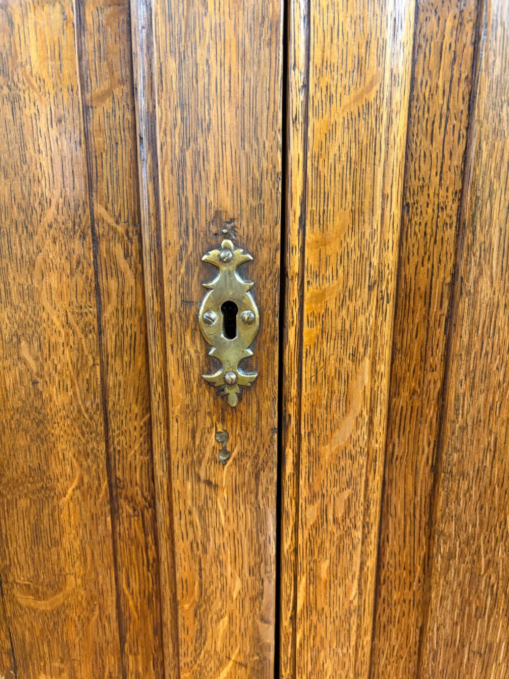 An antique George III oak housekeepers cupboard with arched fielded panels on the top doors above a base of drawers with brass handles. View III