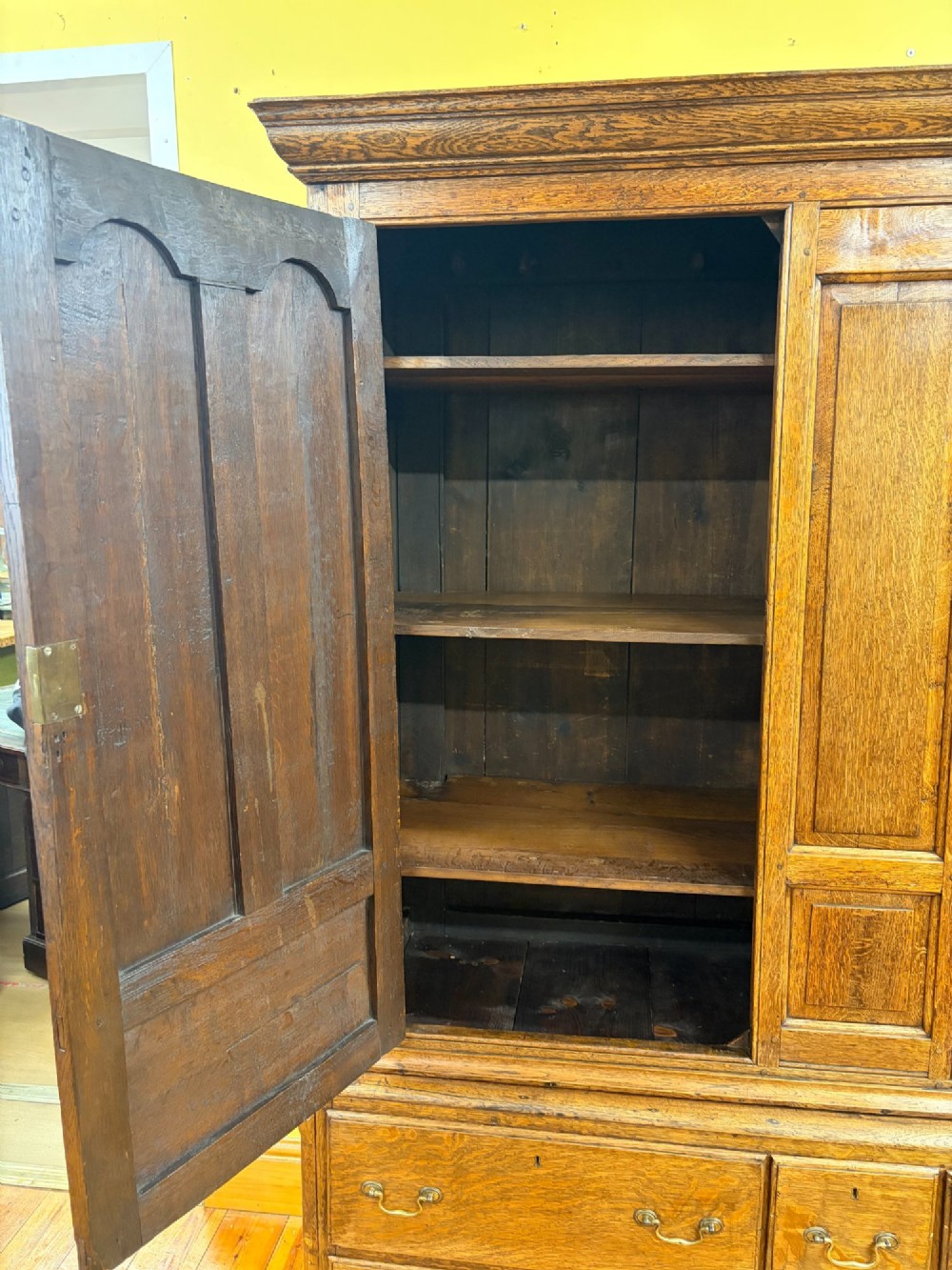 An antique George III oak housekeepers cupboard with arched fielded panels on the top doors above a base of drawers with brass handles. View IV