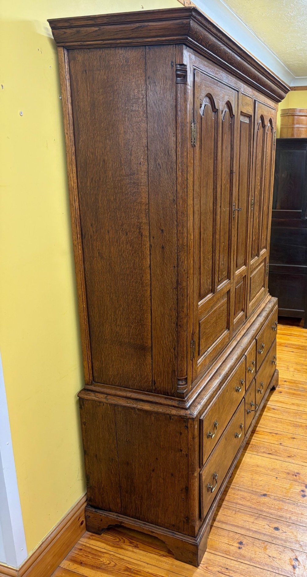 An antique George III oak housekeepers cupboard with arched fielded panels on the top doors above a base of drawers with brass handles. View VI