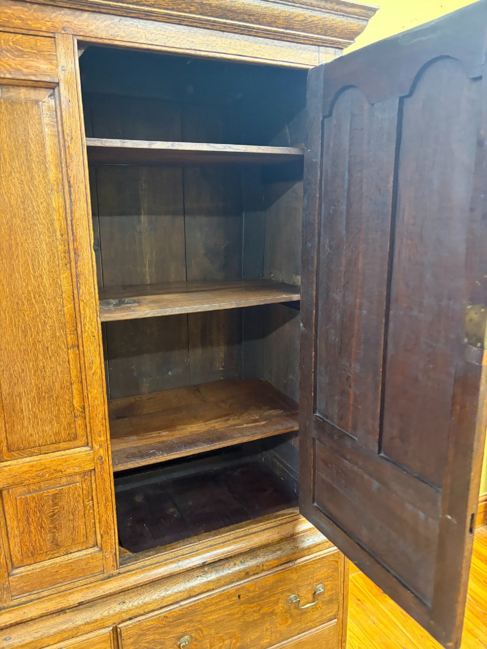 An antique George III oak housekeepers cupboard with arched fielded panels on the top doors above a base of drawers with brass handles. View VIII