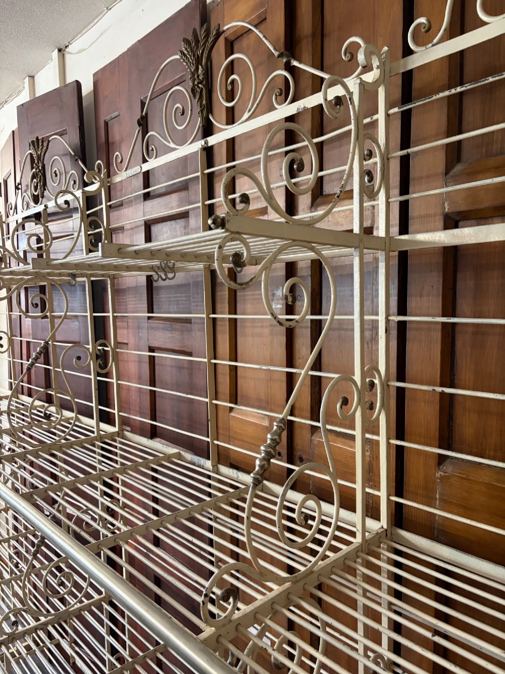 A large, multi-tiered French wrought iron bakers rack painted cream, decorated with scrollwork cresting and brass decorative elements. View VII