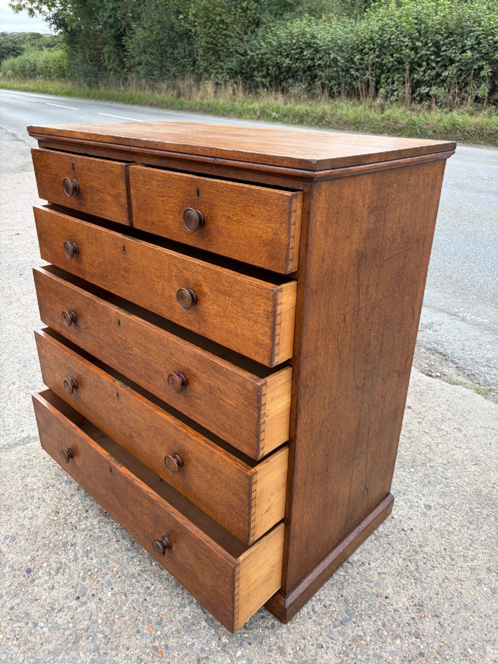 A Victorian warm brown oak chest of drawers featuring two short drawers above four full-width long drawers with turned wooden handles and keyholes. View VII