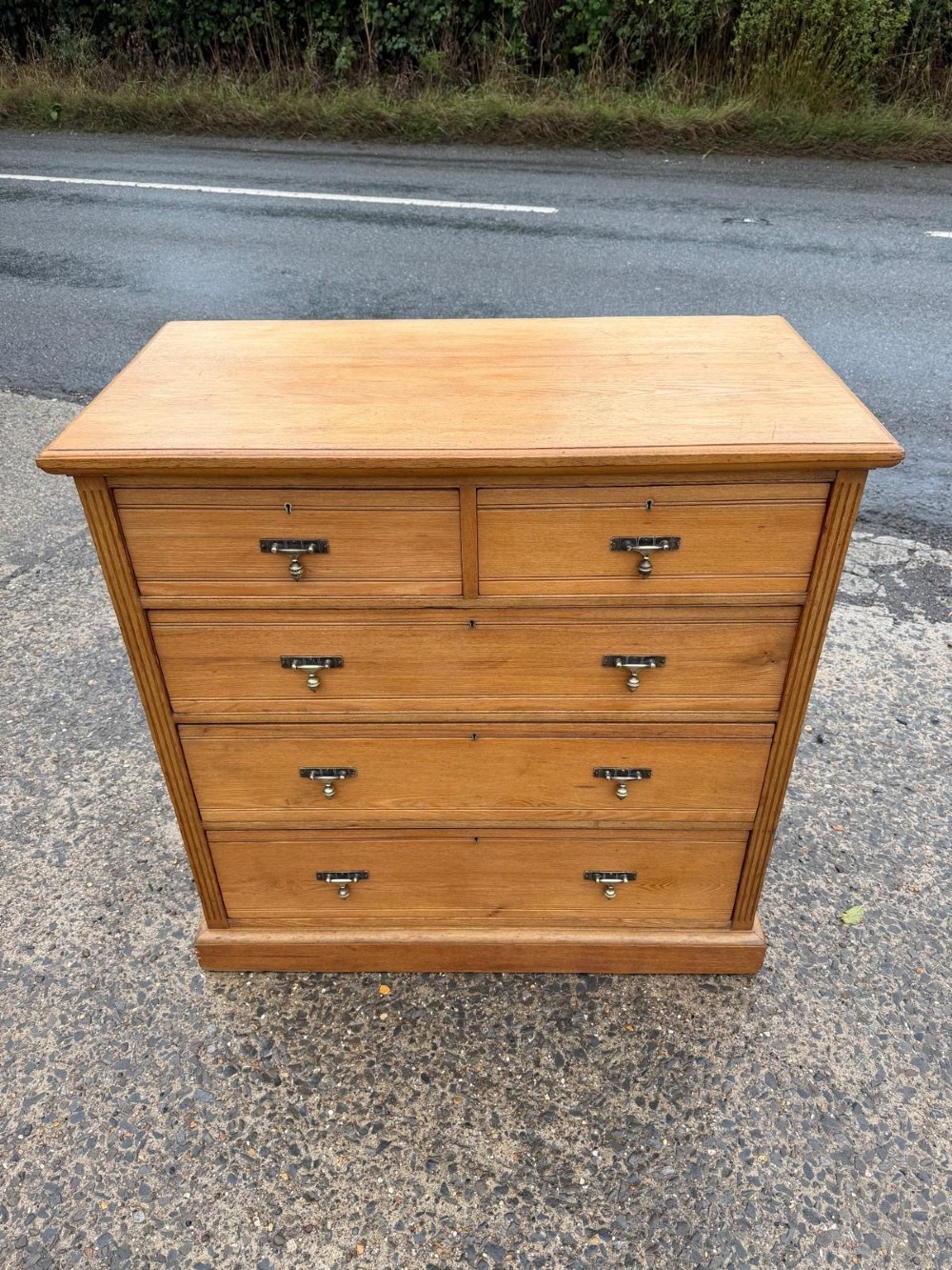 A solid oak chest of drawers featuring a two over three drawer layout with fluted side pilasters and brass acorn drop handles set on a solid base. View VI