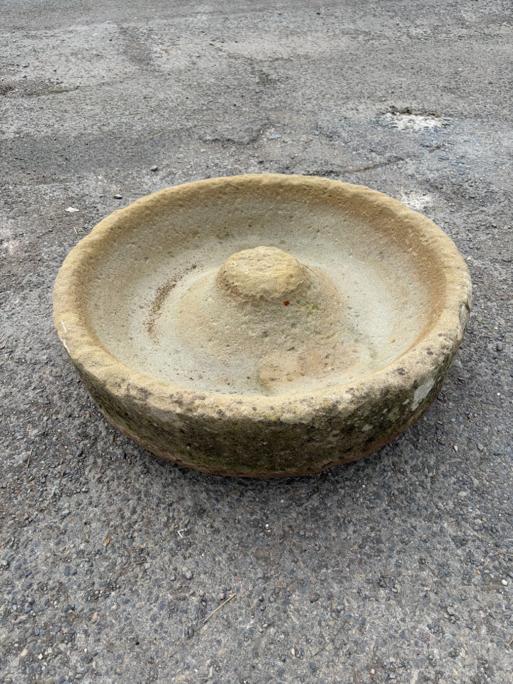 A circular hand-carved antique sandstone pig trough featuring a raised central cone and weathered exterior surface.