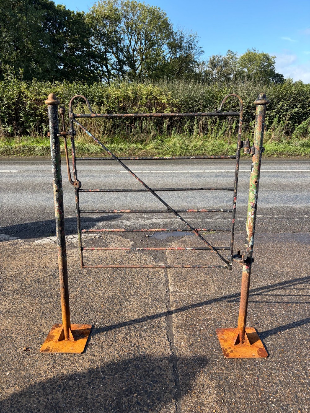 An early 19th-century wrought iron pedestrian field gate with supporting posts, horizontal bars, diagonal bracing, and a weathered paint finish.