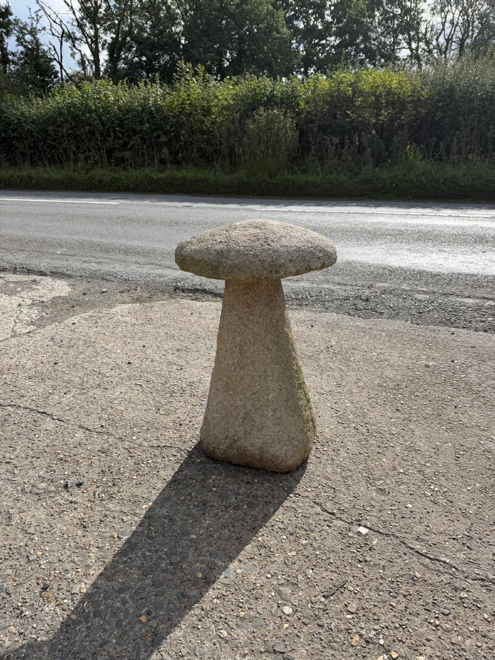 A hand-hewn grey Cornish granite staddle stone with a tapered base and rounded cap resting on a flat surface.