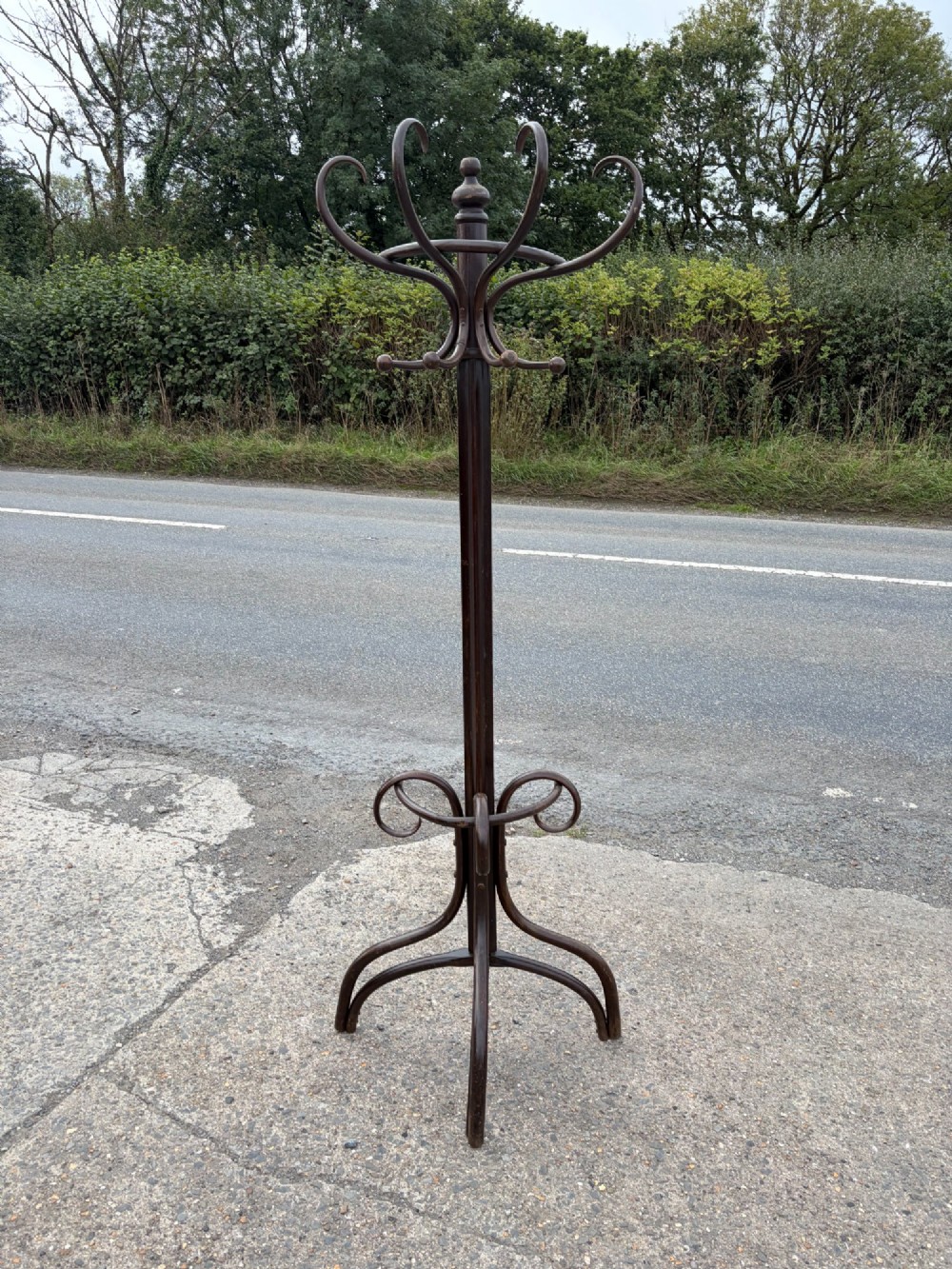 A dark brown bentwood coat stand with curved upper hooks, central accessory loops, a turned finial, and four splayed legs.