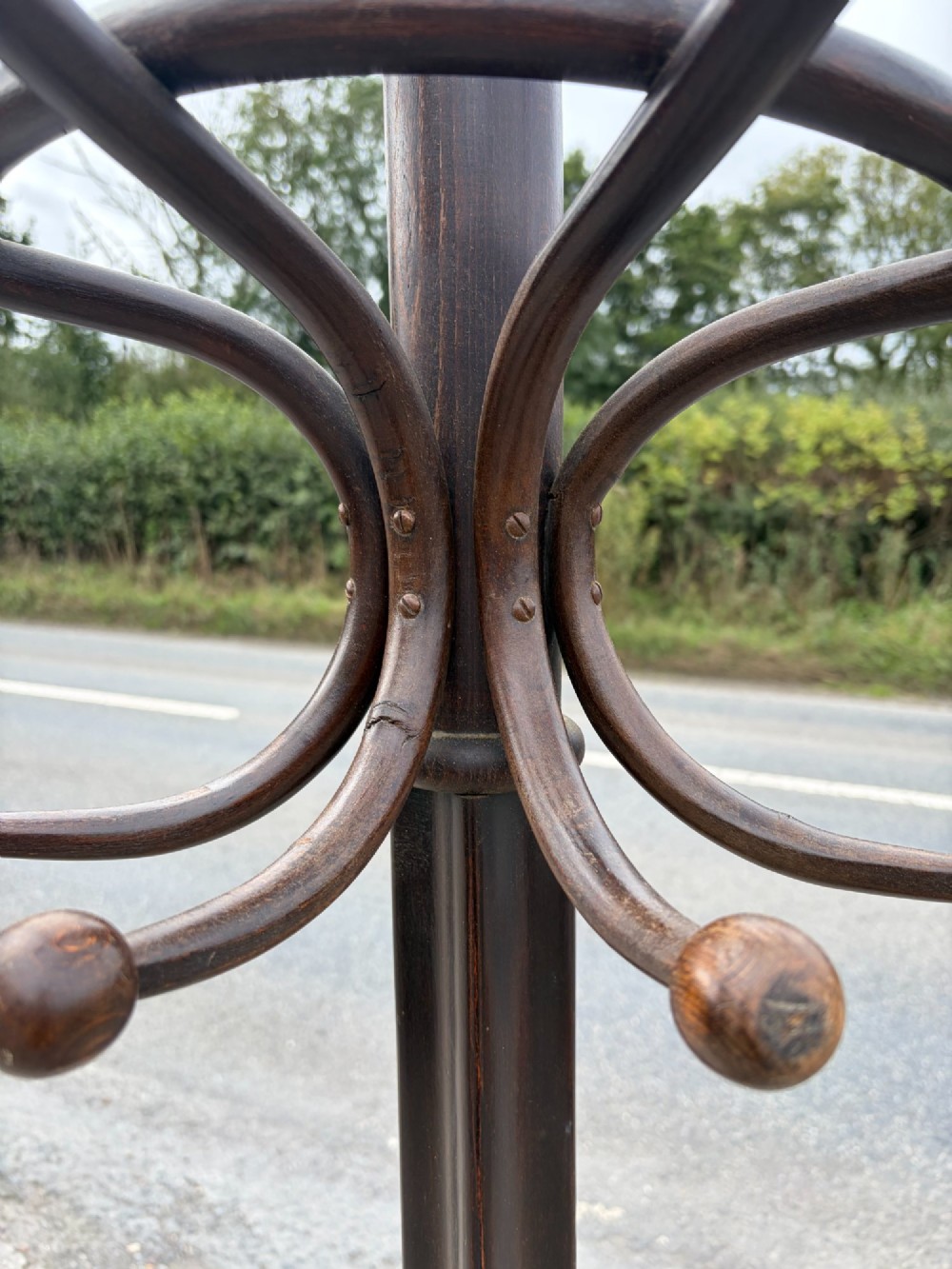 A dark brown bentwood coat stand with curved upper hooks, central accessory loops, a turned finial, and four splayed legs. View III