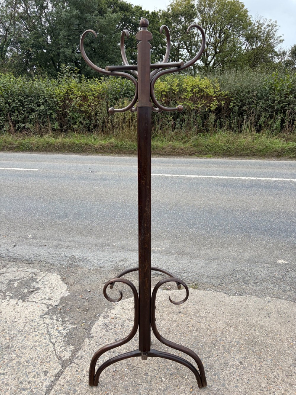 A dark brown bentwood coat stand with curved upper hooks, central accessory loops, a turned finial, and four splayed legs. View VII