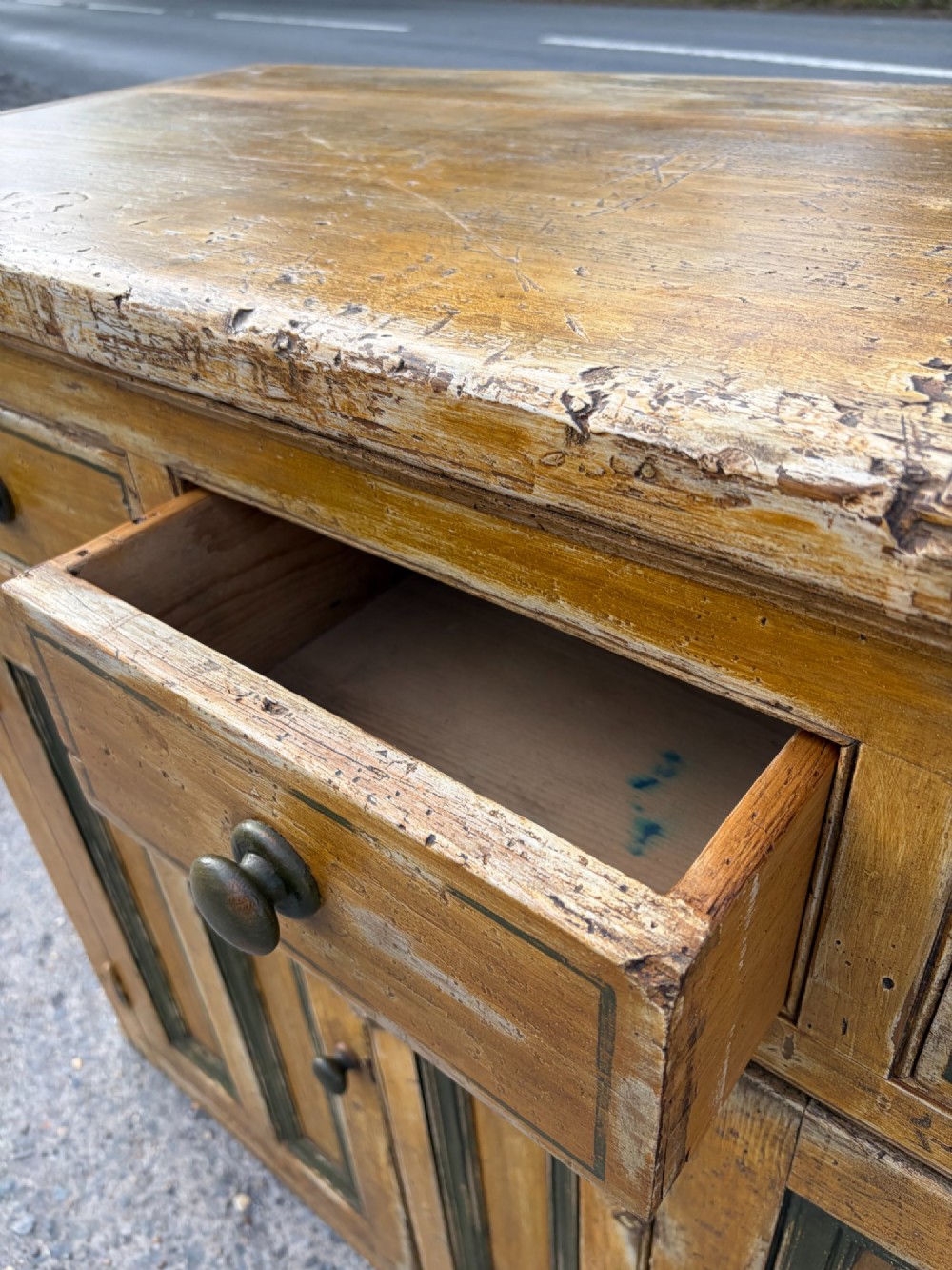 A late Victorian pine dresser base featuring a distressed ochre and green painted finish, three upper drawers, and recessed panel cupboard doors with wooden handles. View V