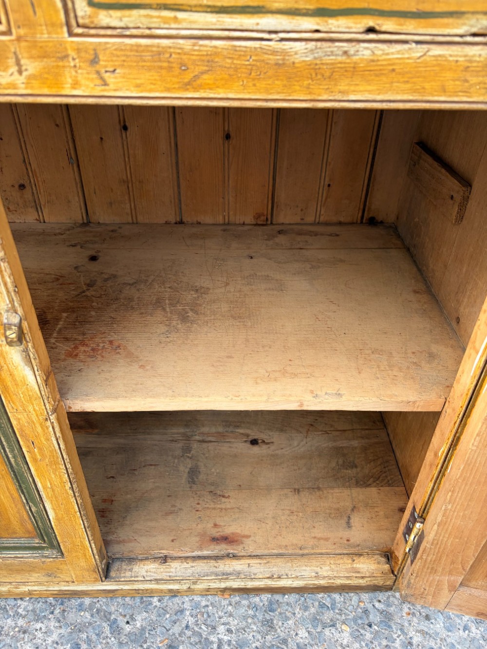 A late Victorian pine dresser base featuring a distressed ochre and green painted finish, three upper drawers, and recessed panel cupboard doors with wooden handles. View VI