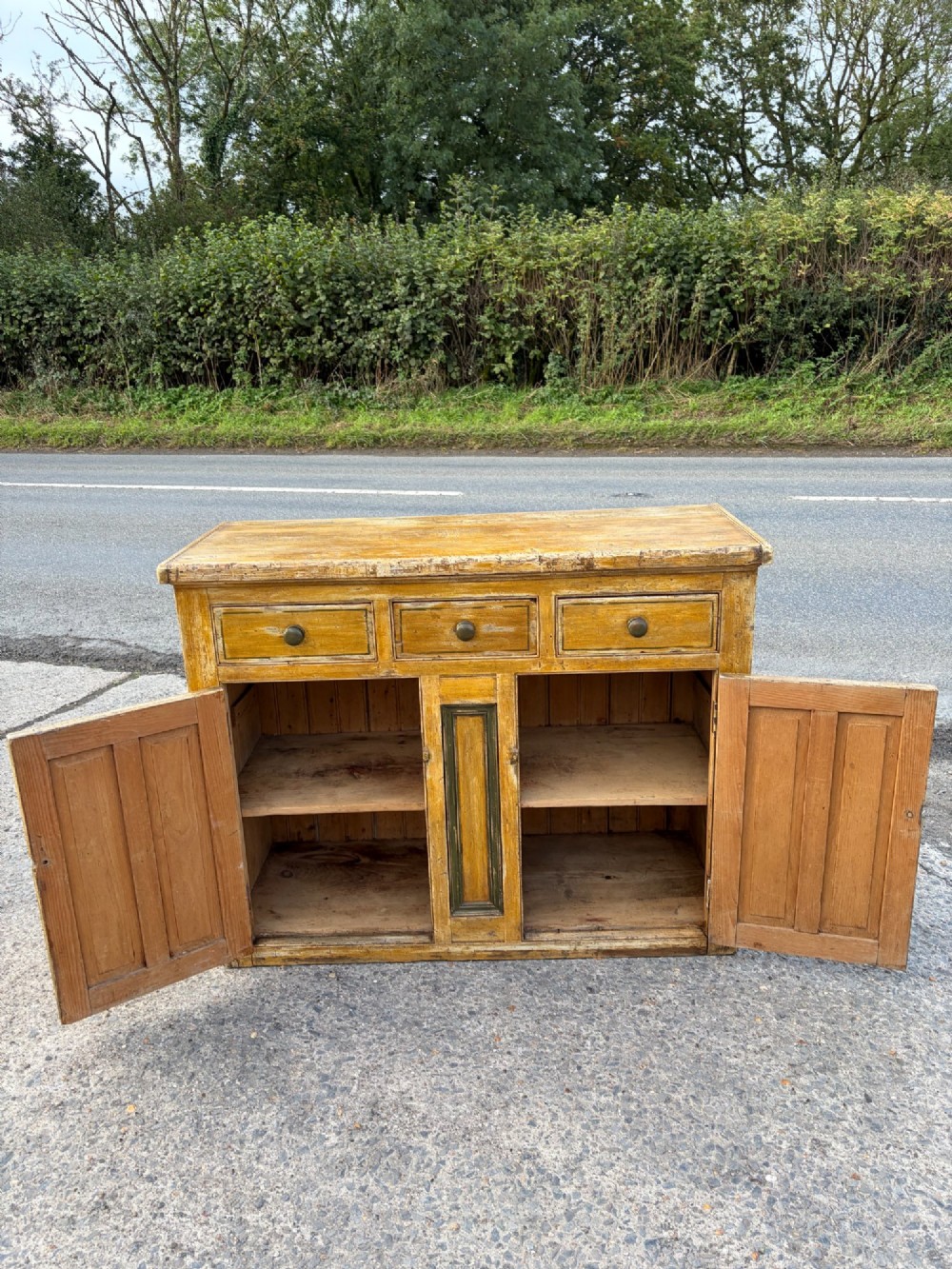 A late Victorian pine dresser base featuring a distressed ochre and green painted finish, three upper drawers, and recessed panel cupboard doors with wooden handles. View VIII