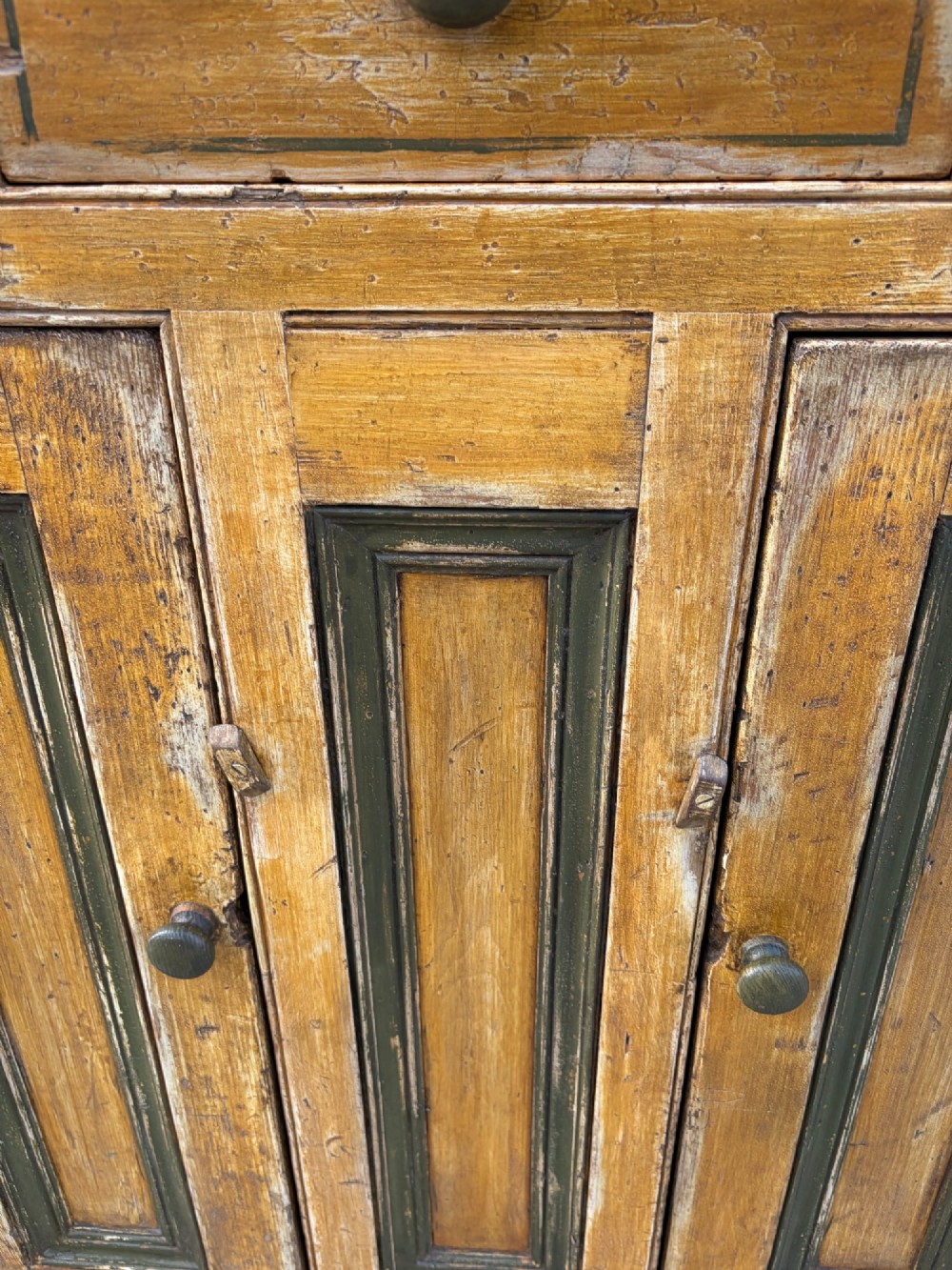 A late Victorian pine dresser base featuring a distressed ochre and green painted finish, three upper drawers, and recessed panel cupboard doors with wooden handles. View IX