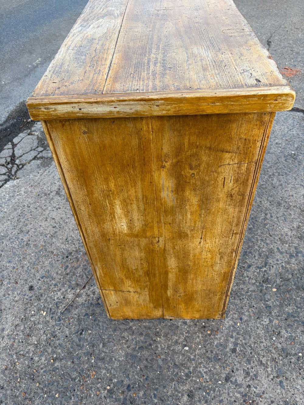 A late Victorian pine dresser base featuring a distressed ochre and green painted finish, three upper drawers, and recessed panel cupboard doors with wooden handles. View XI
