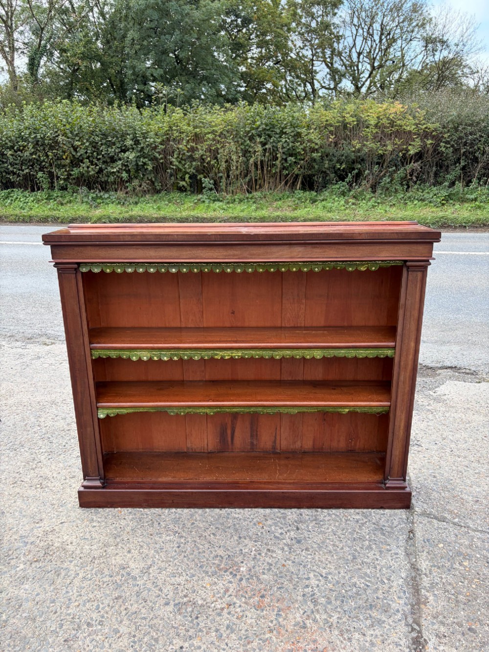 A matching pair of low, open-front early Victorian mahogany bookcases featuring green scalloped leather dust flaps along the shelf edges. View II