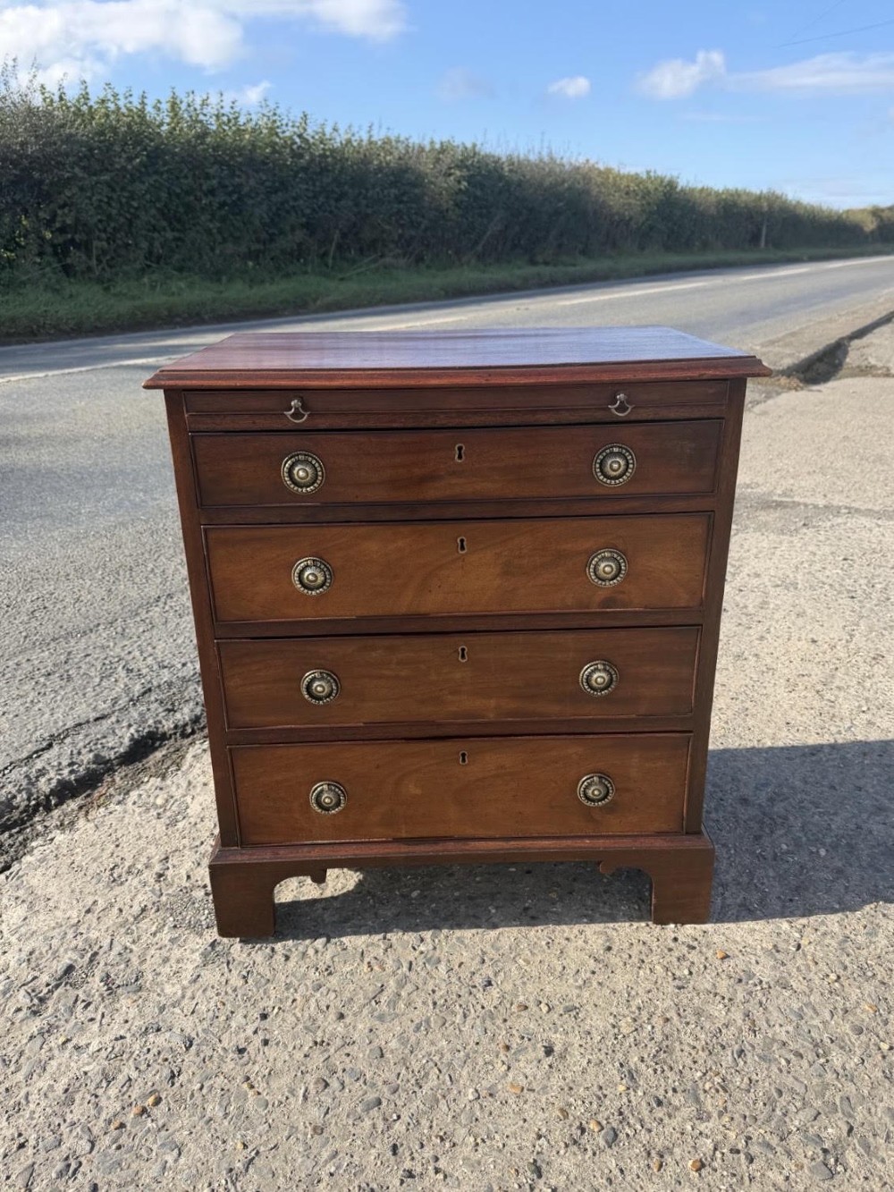 An antique Georgian mahogany bachelors chest featuring four graduated drawers with brass handles, a pull-out brushing slide, and bracket feet.