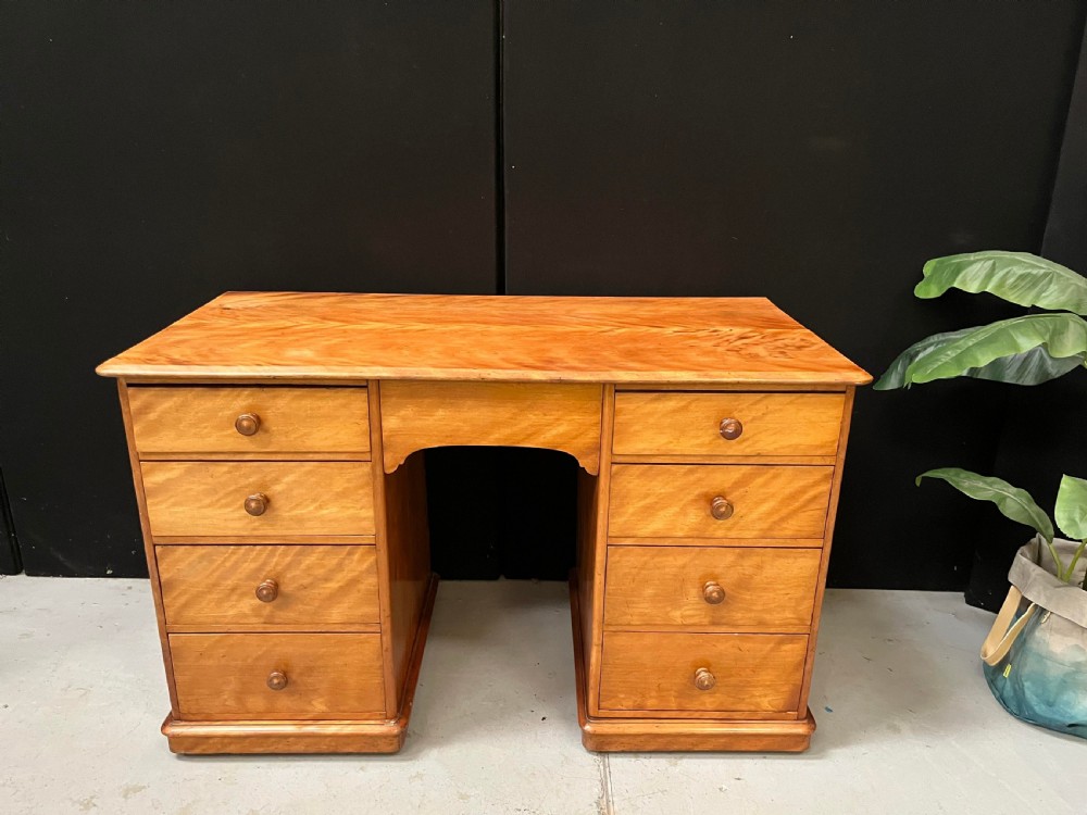 A Victorian satin birch pedestal writing desk featuring eight drawers with turned wooden knobs and an arched central kneehole.