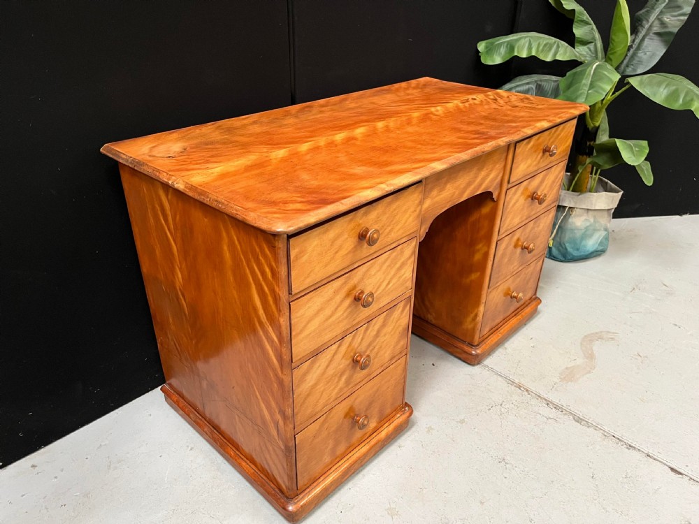 A Victorian satin birch pedestal writing desk featuring eight drawers with turned wooden knobs and an arched central kneehole. View III