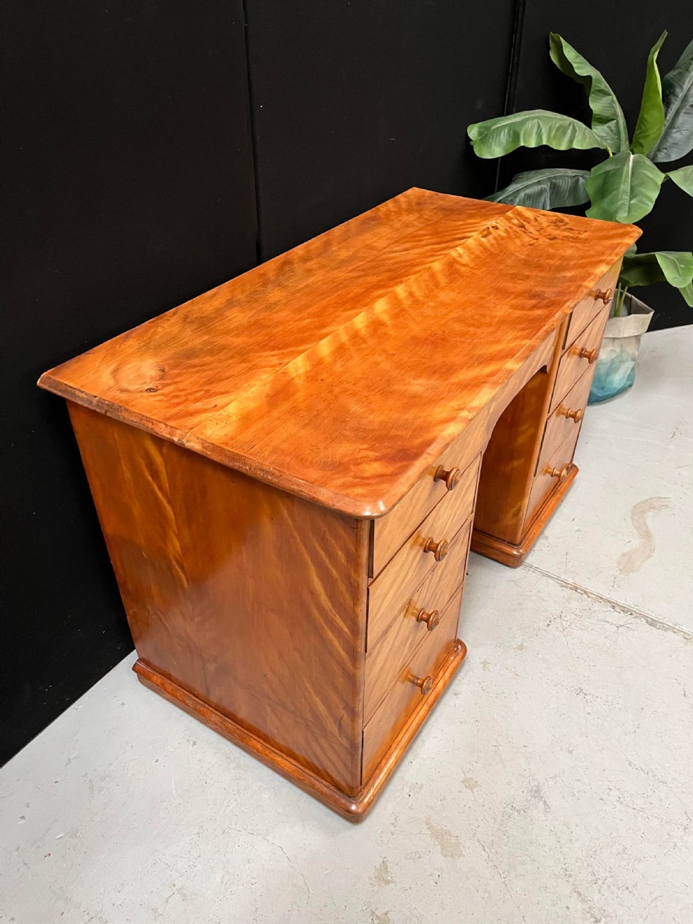 A Victorian satin birch pedestal writing desk featuring eight drawers with turned wooden knobs and an arched central kneehole. View V
