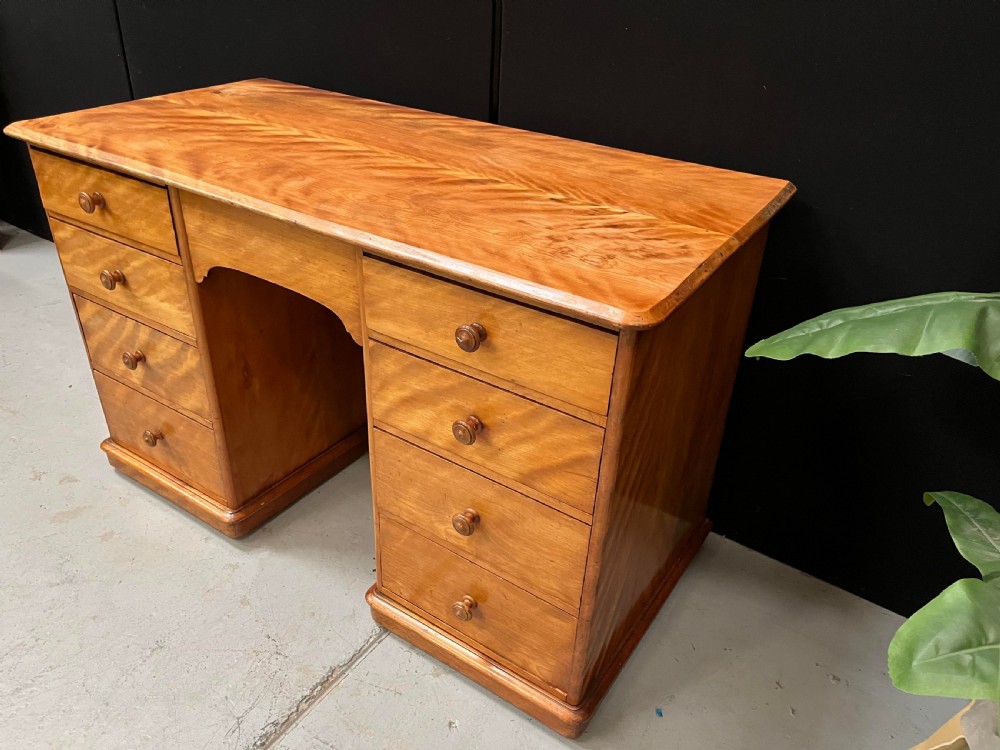 A Victorian satin birch pedestal writing desk featuring eight drawers with turned wooden knobs and an arched central kneehole. View VI