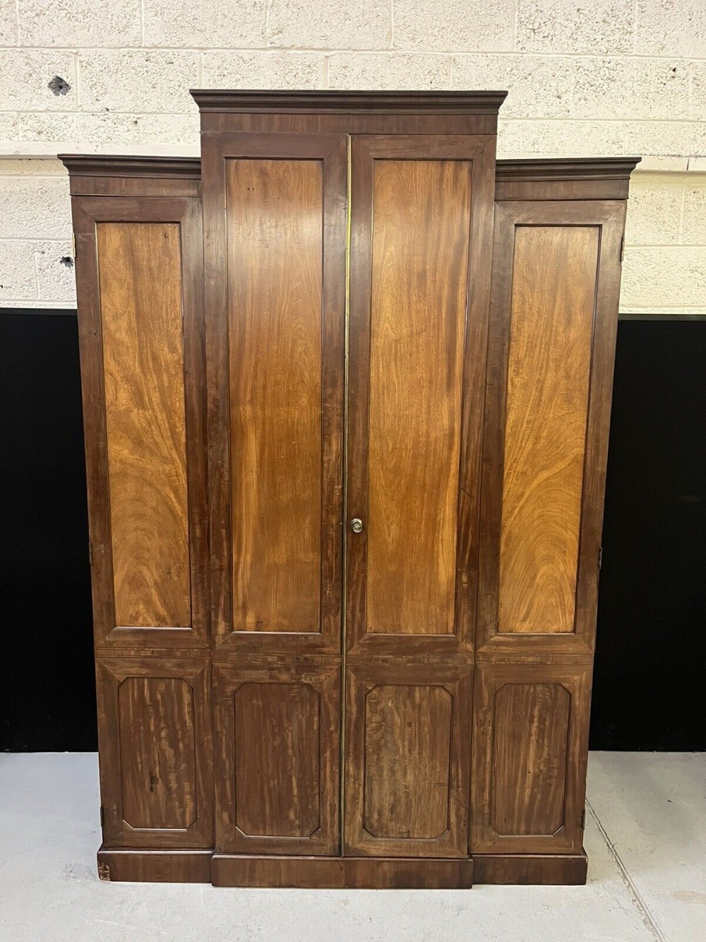 A large mahogany breakfront wardrobe featuring four panelled doors with flame mahogany veneers and stepped moulded cornices.