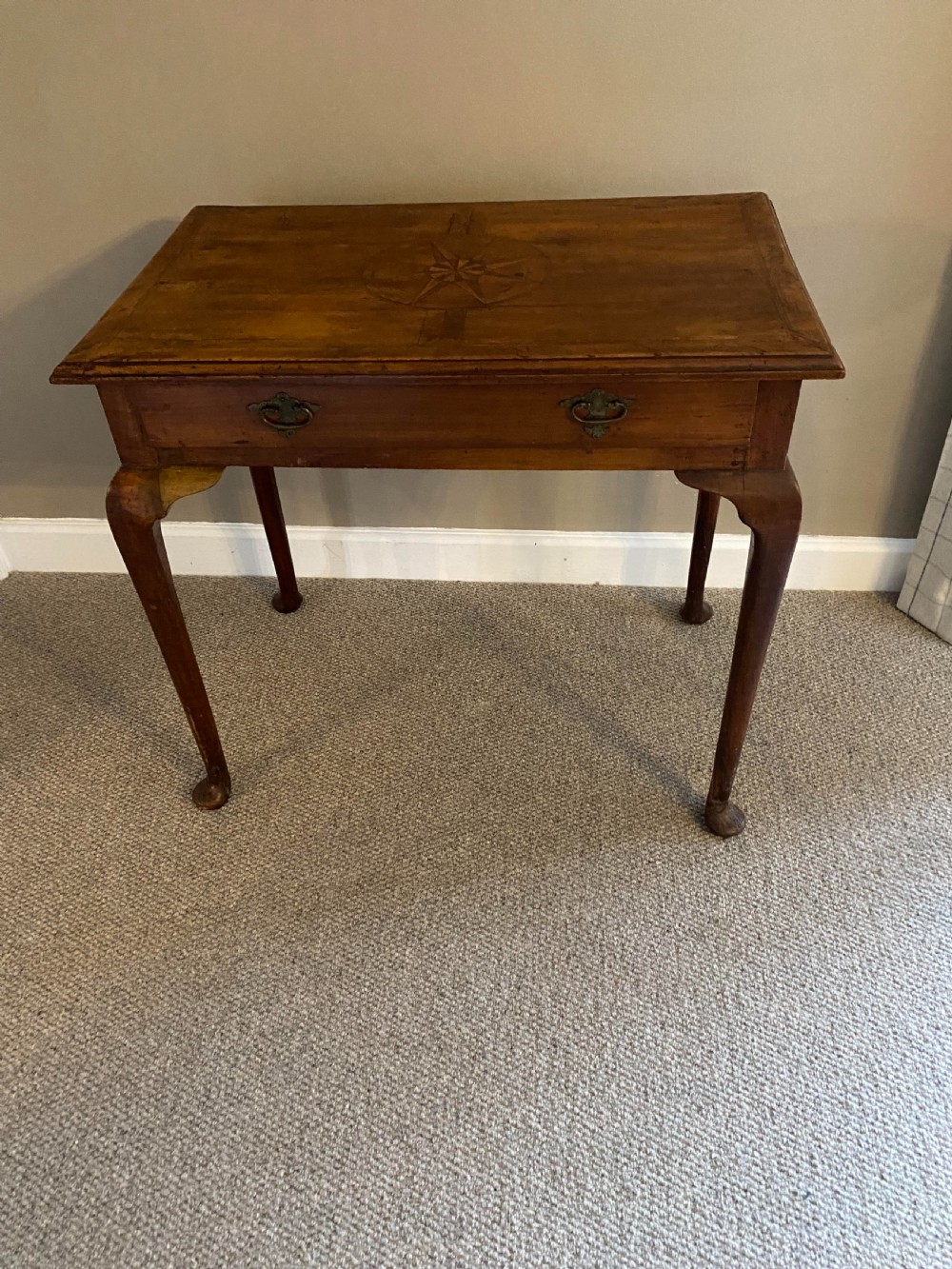 A Georgian fruitwood side table featuring cabriole legs with pad feet, a single drawer with brass handles, and a central star compass inlay on the tabletop.