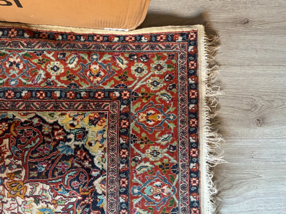 A hand-knotted Persian Kashan rug featuring a central floral medallion on a cream field with a crimson red border. View VI