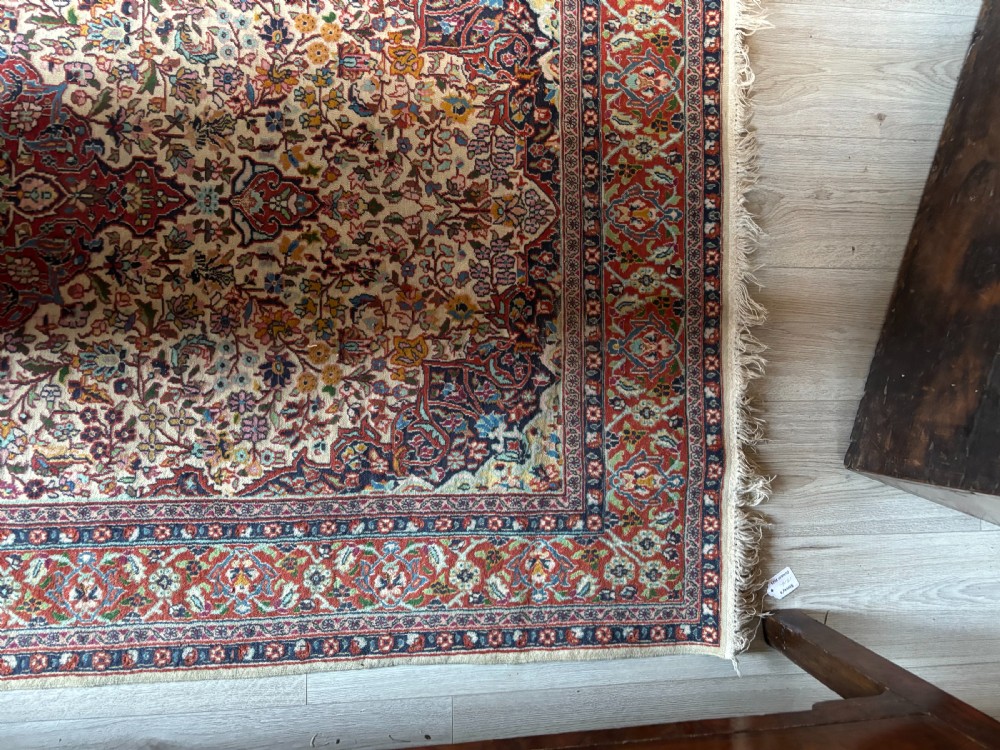 A hand-knotted Persian Kashan rug featuring a central floral medallion on a cream field with a crimson red border. View VII